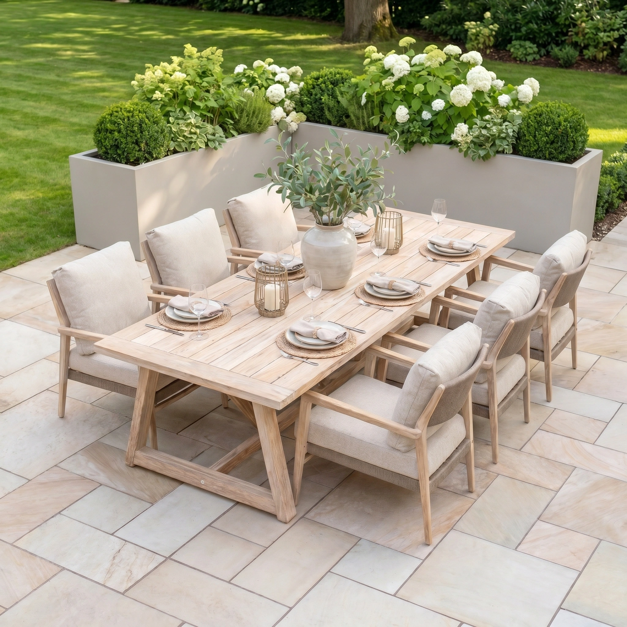 The Noah 6 Seat Low Rectangular Dining Set in Volga Grey, inspired by the 4 Seasons Rope collection, is arranged on a stone patio next to green grass and white flowers.