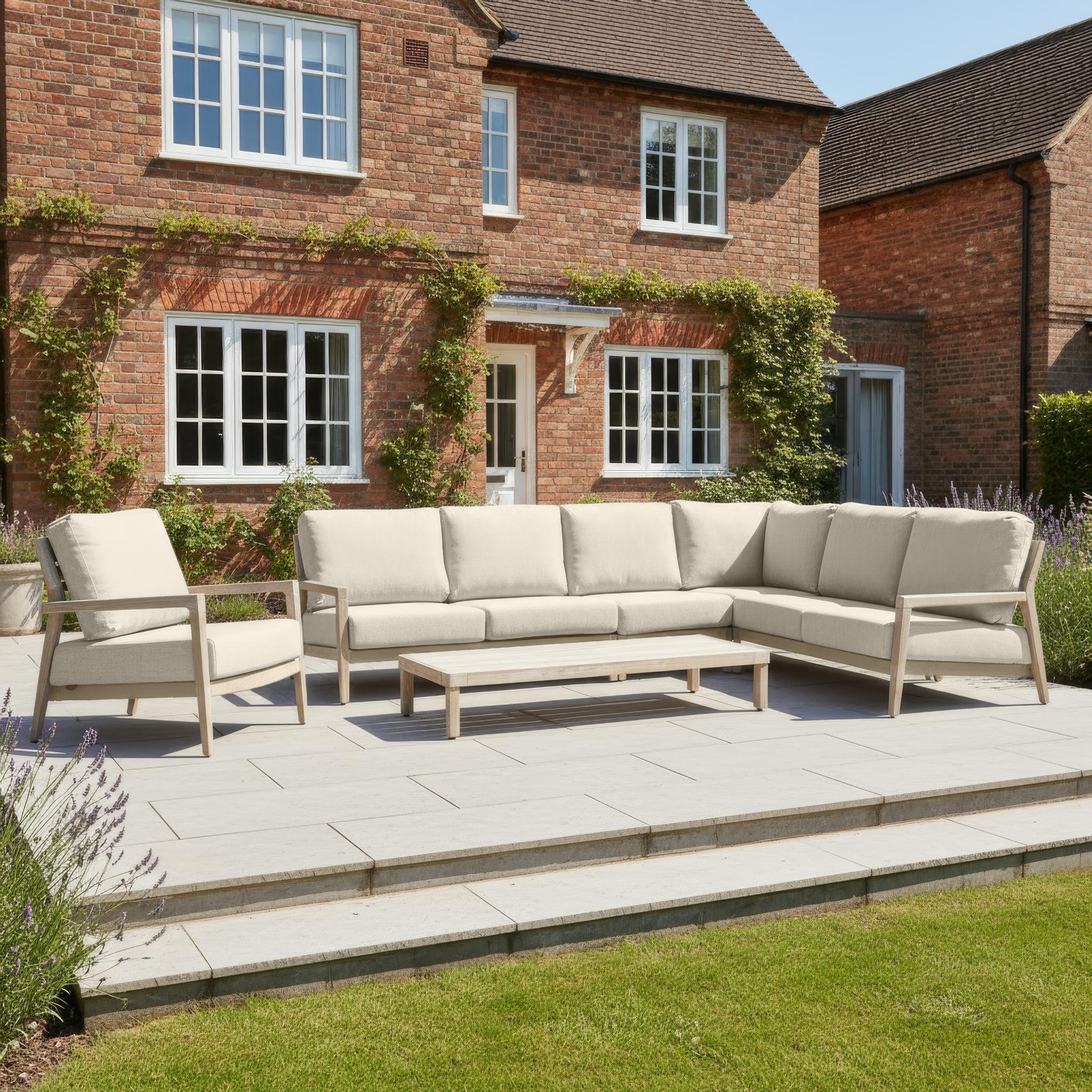 Noah Corner Sofa Set with Armchair in Volga Grey arranged with a chair and table on a stone patio in front of a brick house with windows.