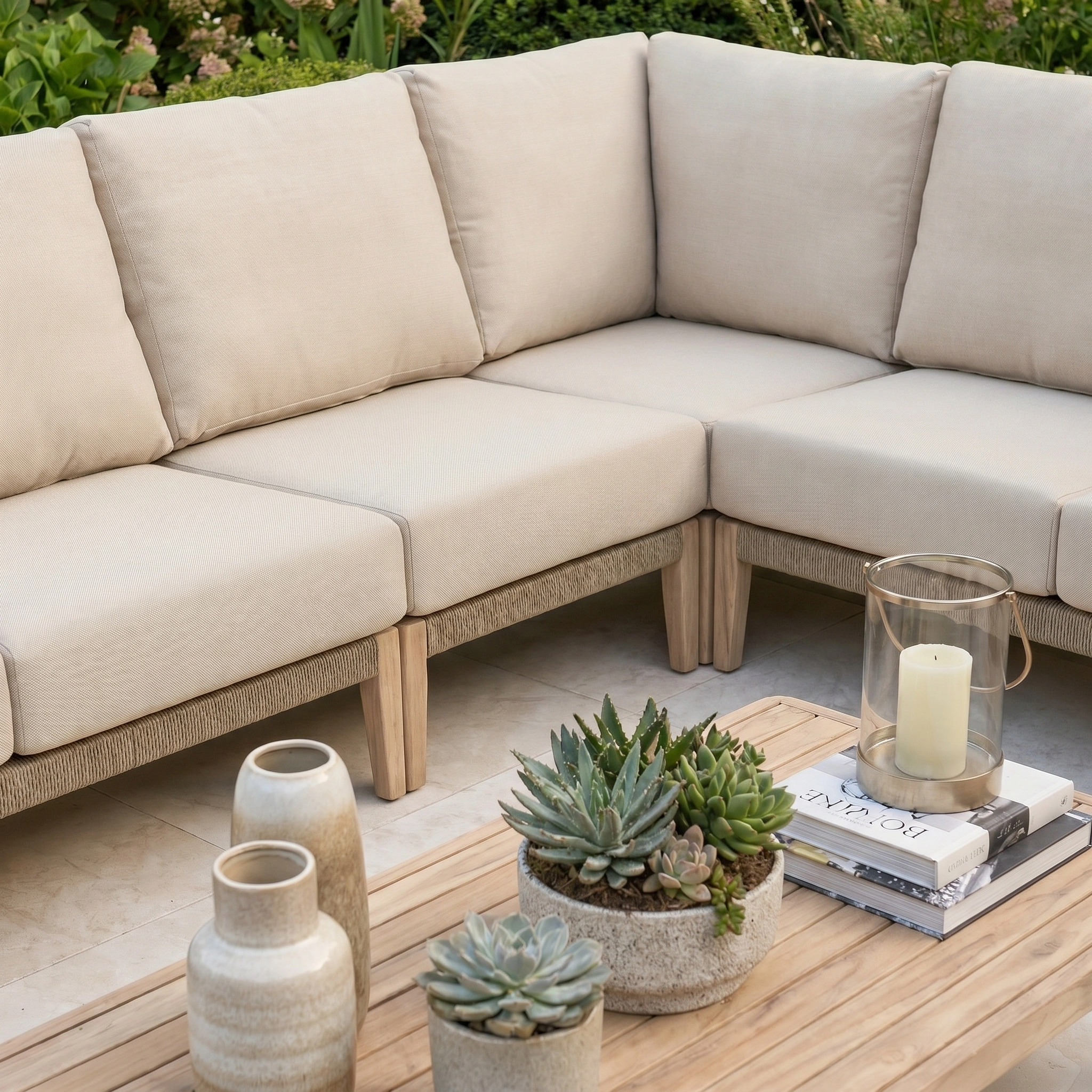 The Noah Corner Sofa Set in Volga Grey, with beige cushions and wooden legs, creates a cozy patio retreat when surrounded by plants and decor.