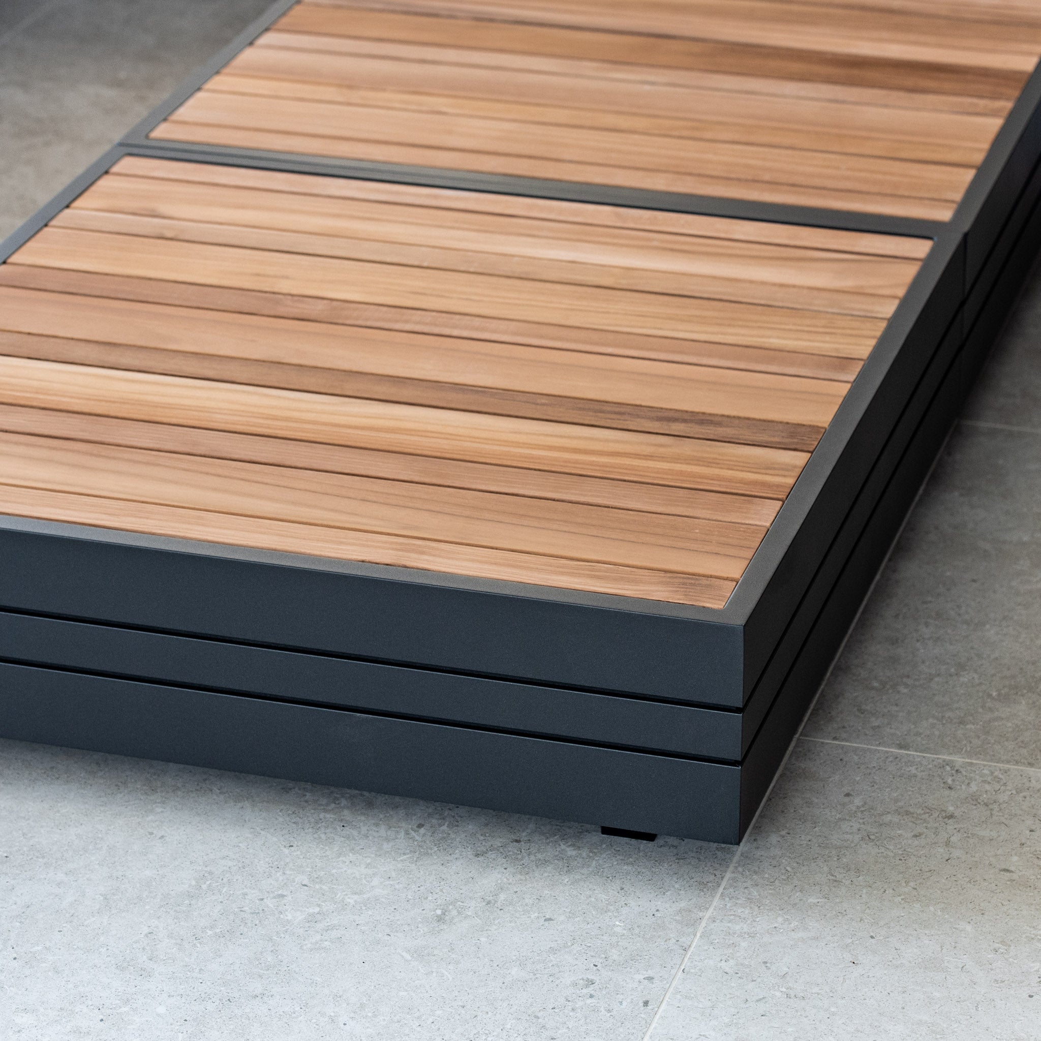 Close-up of a low wooden bench with a dark gray frame on a light stone tile floor, showcasing the exquisite craftsmanship reminiscent of the Panama Luxury Outdoor Large U-Shape Corner Sofa Set in Washed Grey by Harbour Lifestyle.