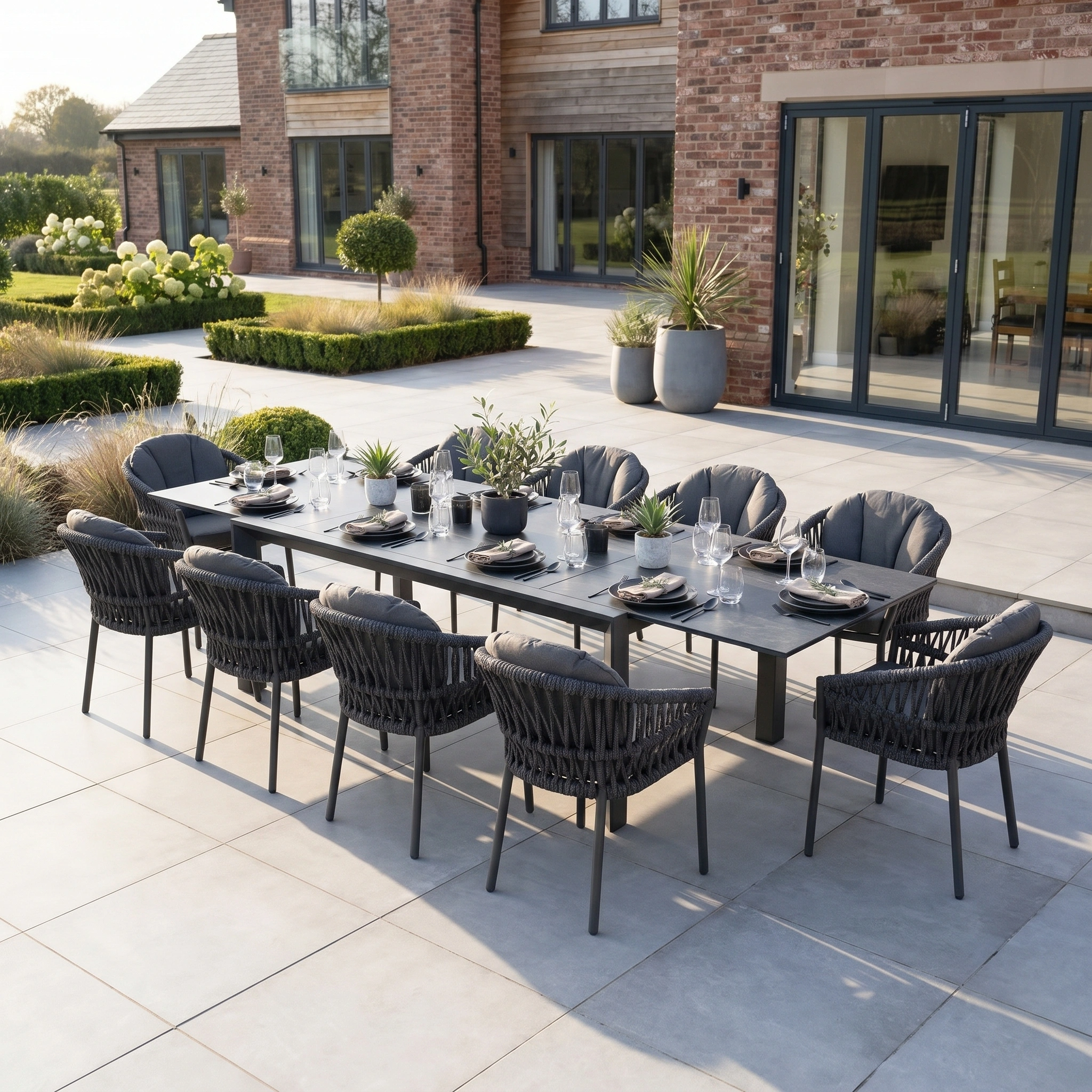 The Pello 10 Seat Extending Dining Set with Ceramic Table in Grey features modern dark grey chairs and an extendable table, ideal for outdoor gatherings on a tiled patio.