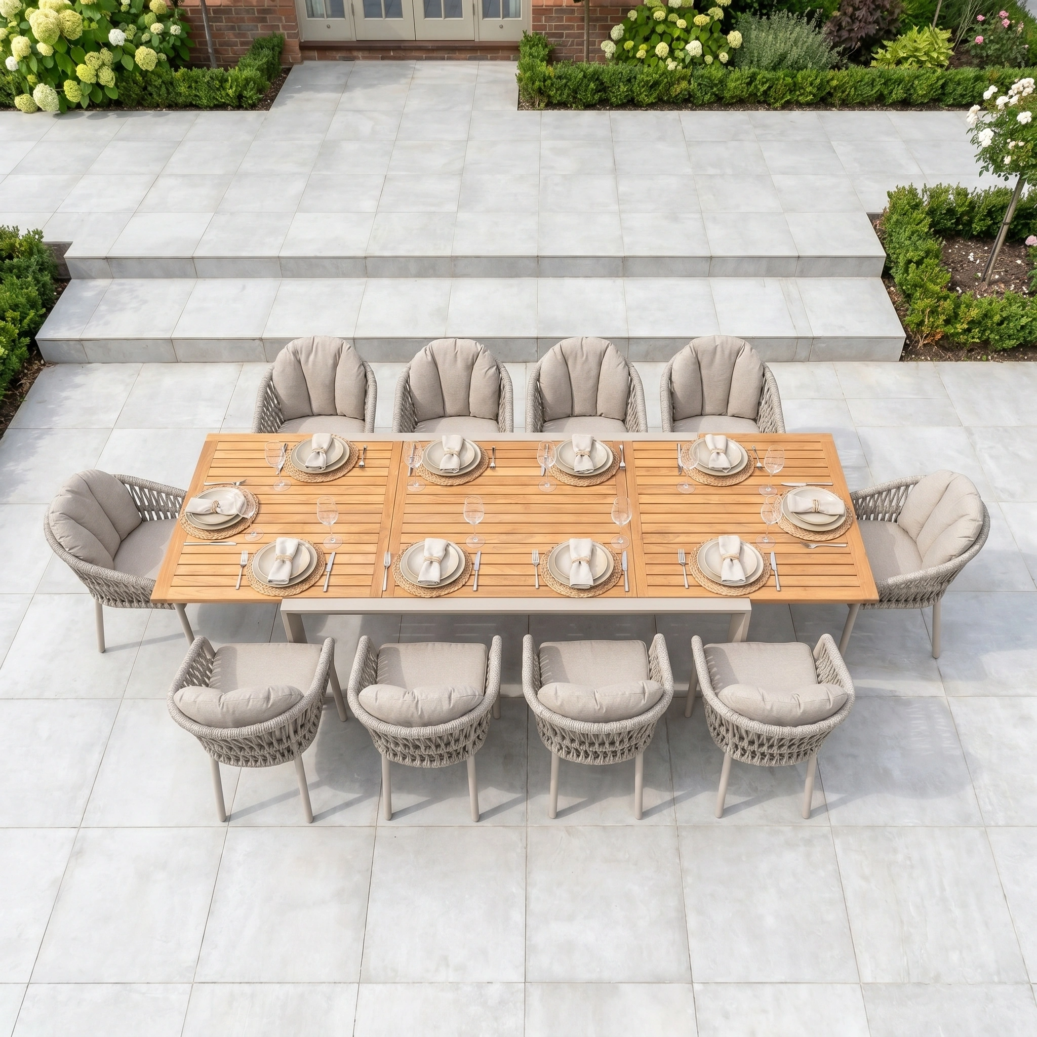 The Pello 10 Seat Extending Dining Set features a teak table and ten cushioned chairs, arranged with plates and cups—ideal for gatherings on a stylish tiled patio.