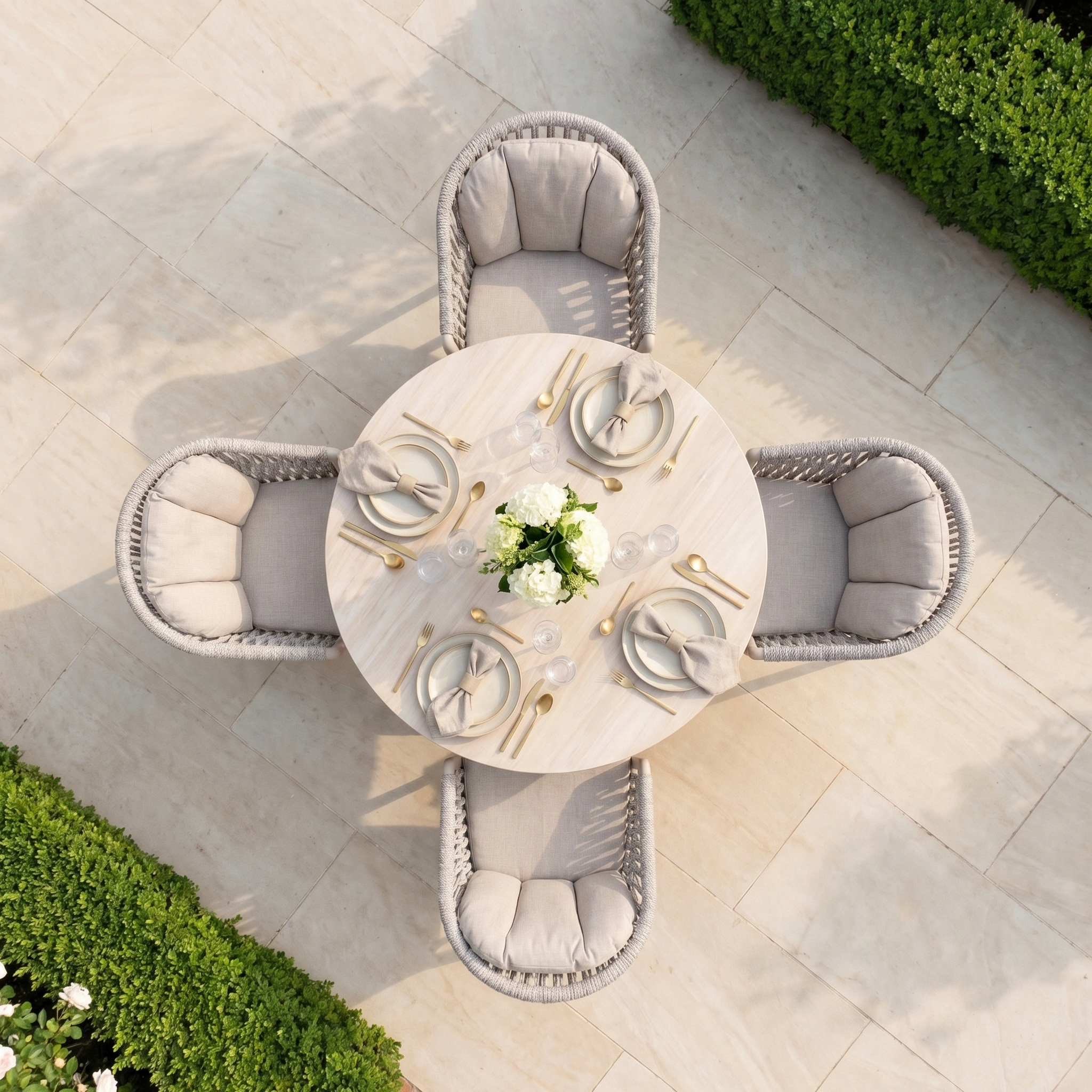 The Pello 4 Seat Round Dining Set with Albatross Table in Fawn features neutral chairs and a stylish table, accented with white flowers and greenery for a chic outdoor dining space.