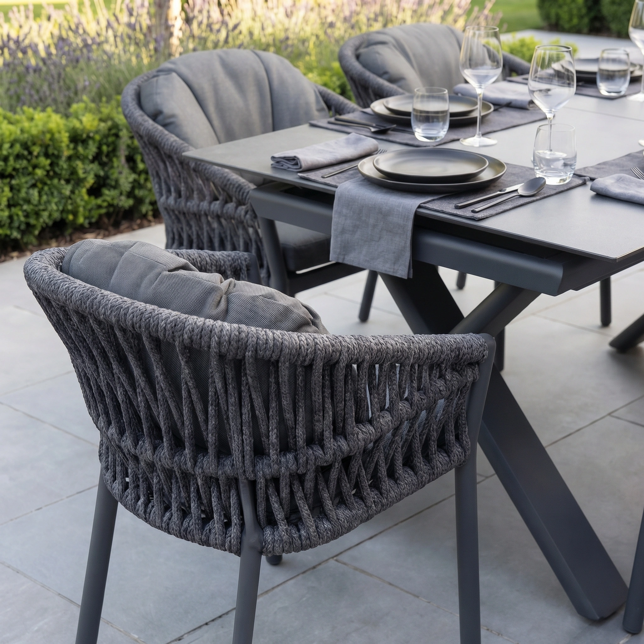 The Pello 6 Seat Dining Set with Albatross Extending Table in Grey includes woven chairs, grey cushions, plates, glasses, and napkins—ideal for stylish outdoor dining on your patio.