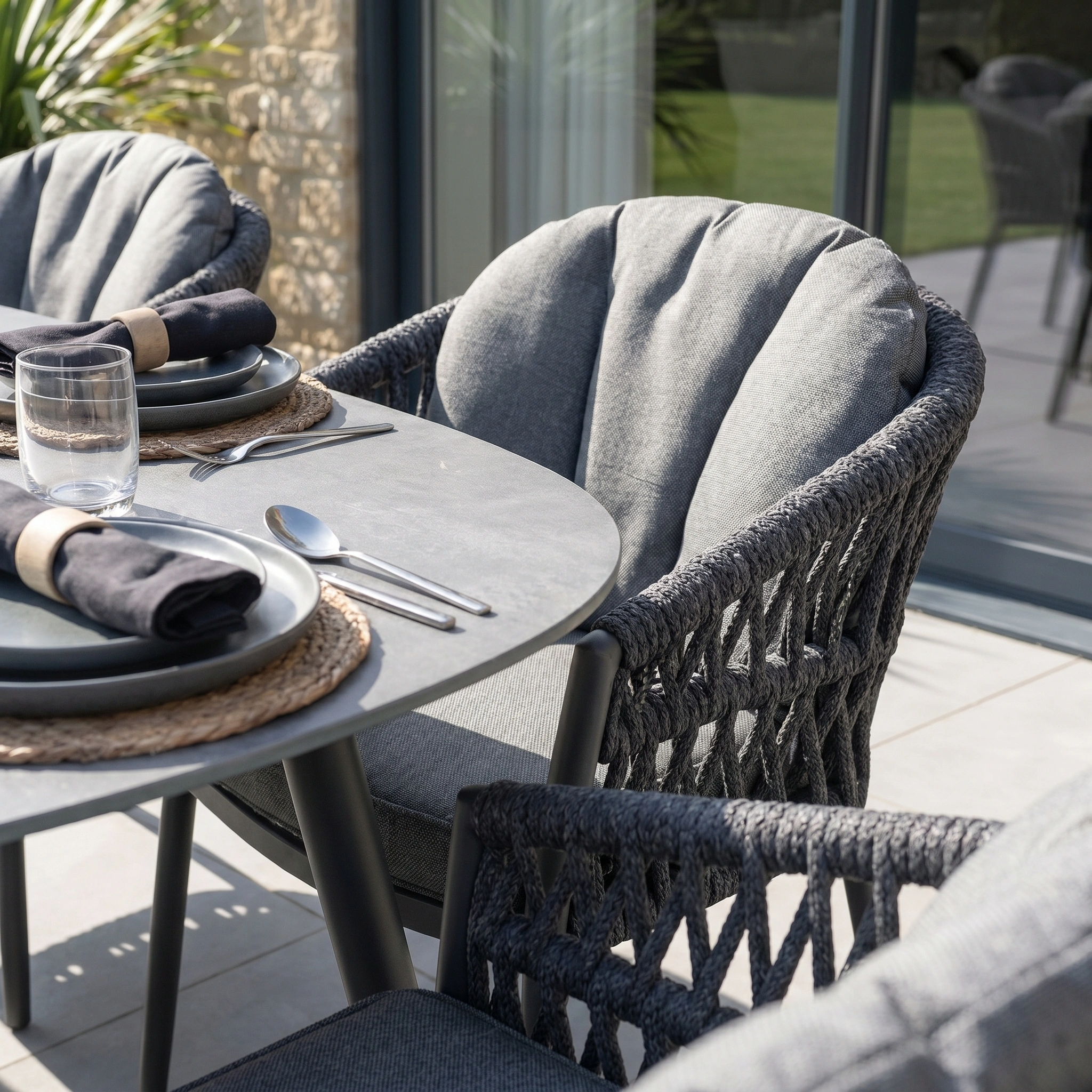 The Pello 6 Seat Oval Dining Set with Ceramic Table in Grey features stylish grey chairs and a spacious table—ideal garden patio furniture for outdoor dining on sunny days, complete with plates, glasses, and napkins.