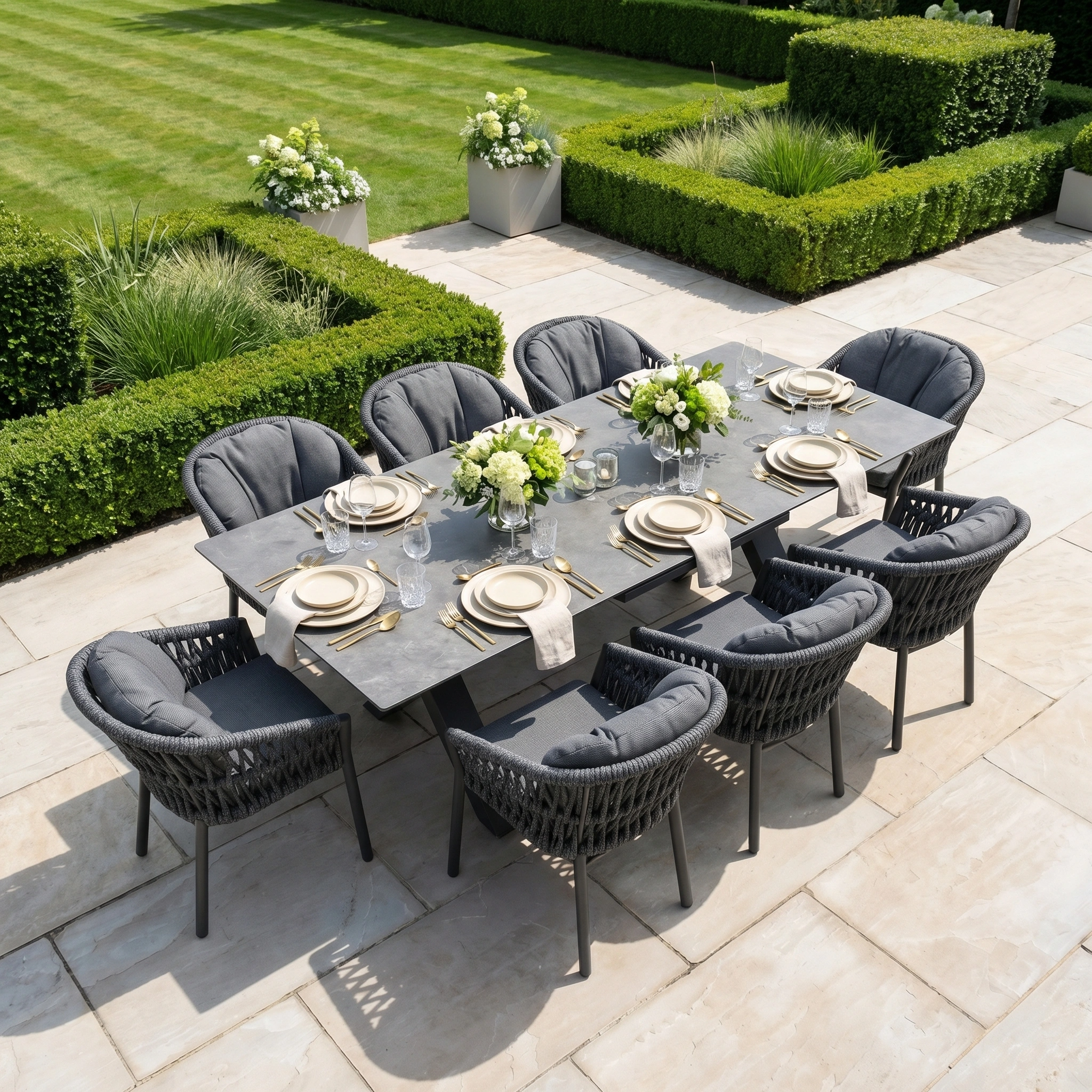 The Pello 8 Seat Dining Set with Albatross Extending Table in Grey features eight garden chairs, plates, glasses, and white floral centerpieces—an elegant choice for stylish outdoor gatherings.