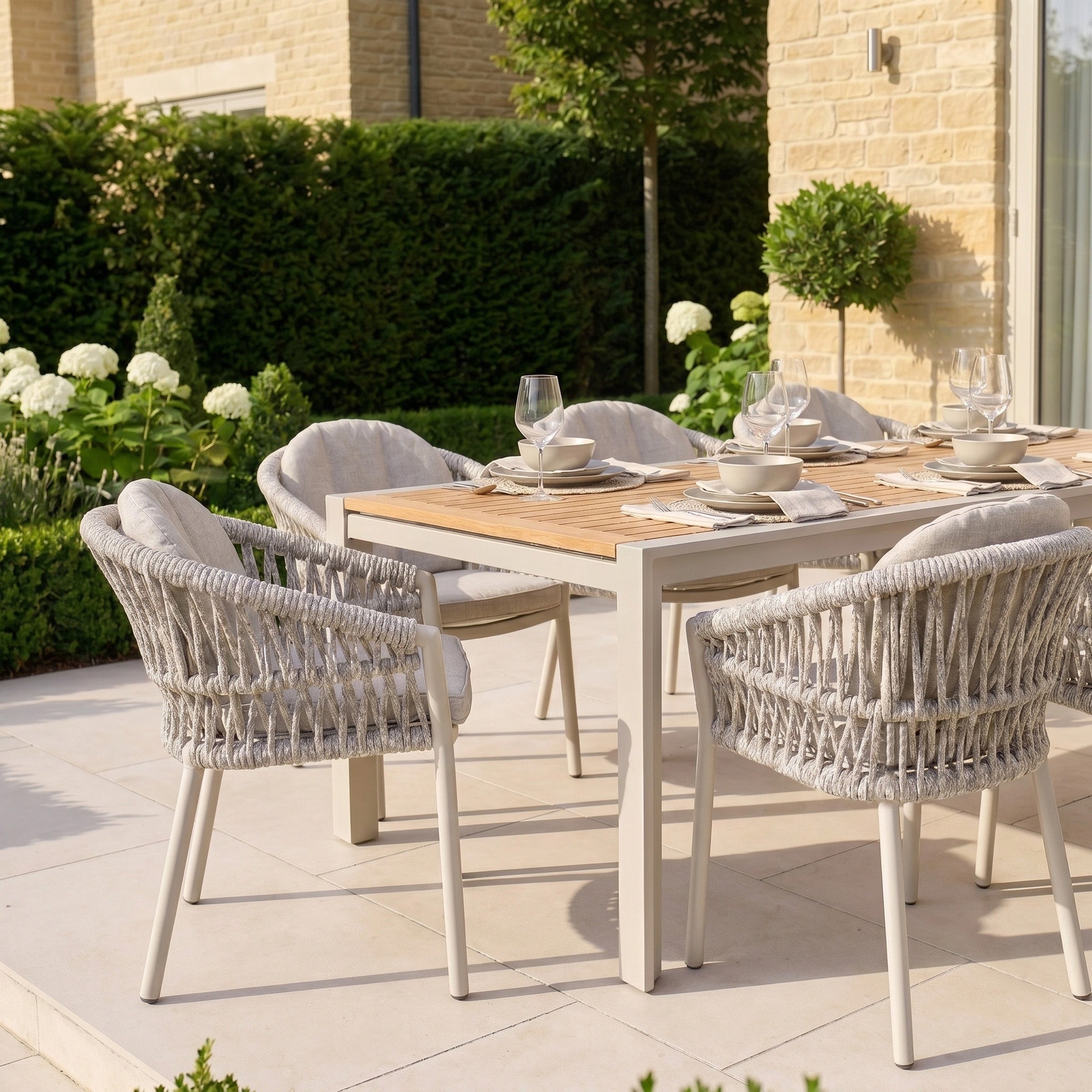 The Pello 8 Seat Extending Dining Set with Teak Table in Fawn offers weather-resistant style and durability, featuring an extendable teak table and chairs—perfect for alfresco dining amid patio greenery and flowers.