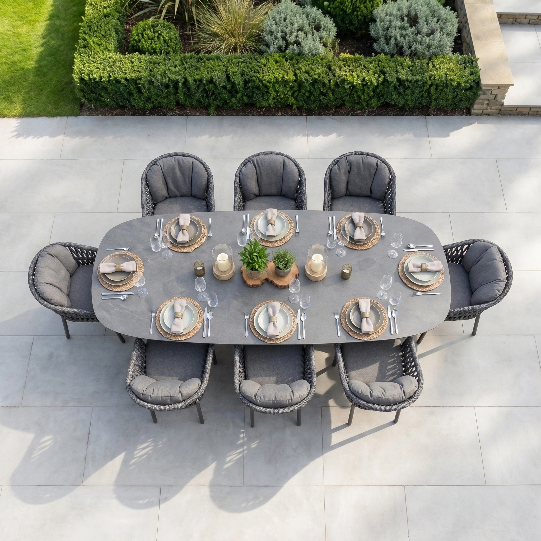 The Pello 8 Seat Oval Dining Set with Albatross Extending Table in Grey features weather-resistant gray cushioned chairs and a spacious extending table, perfect for outdoor dining. Includes plates, glasses, and centerpiece plants.