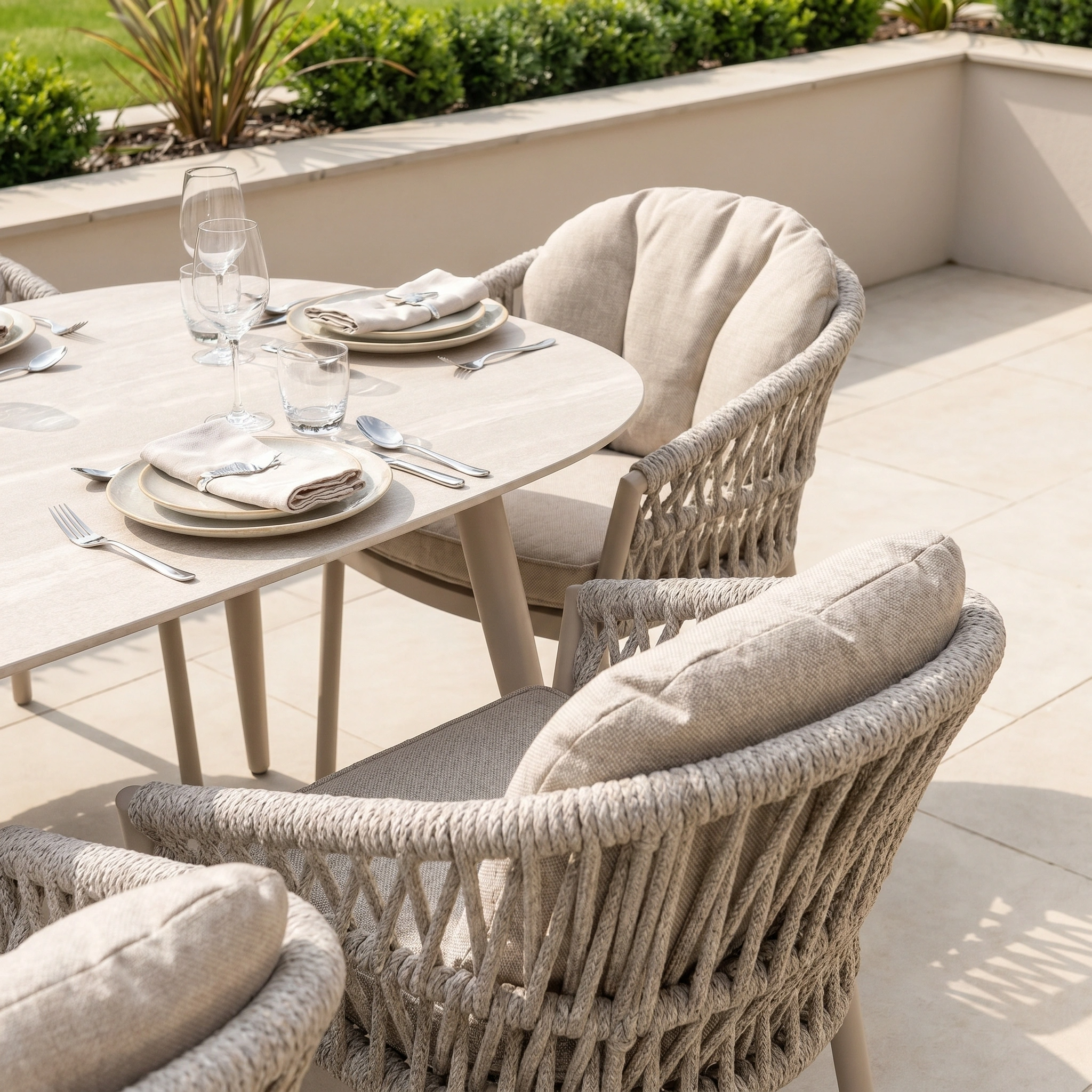 The Pello 8 Seat Oval Dining Set with Ceramic Table in Fawn features elegant woven chairs and tableware on a tiled patio—a stylish, weather-resistant choice for outdoor dining and entertaining.