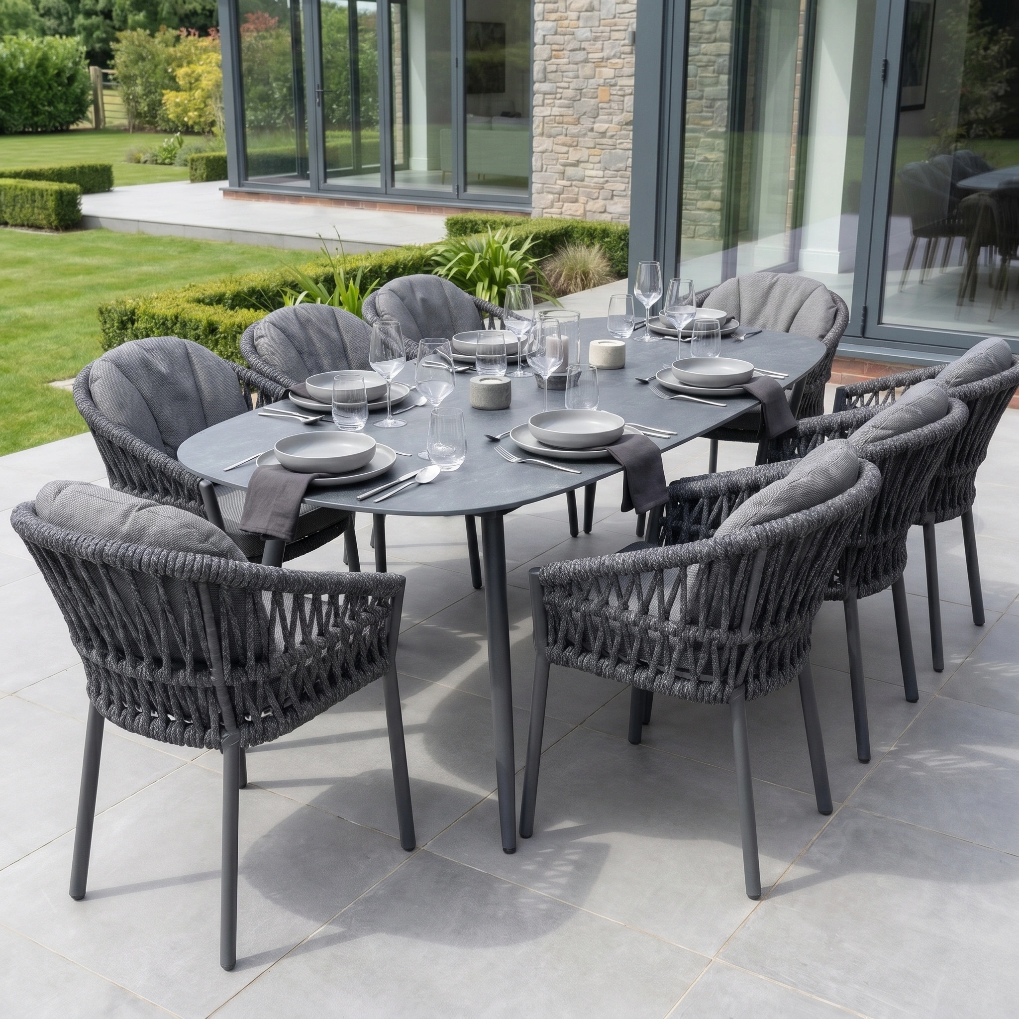 The Pello 8 Seat Oval Dining Set with Ceramic Table in Grey features weather-resistant woven patio furniture, set for dining on a stylish patio.