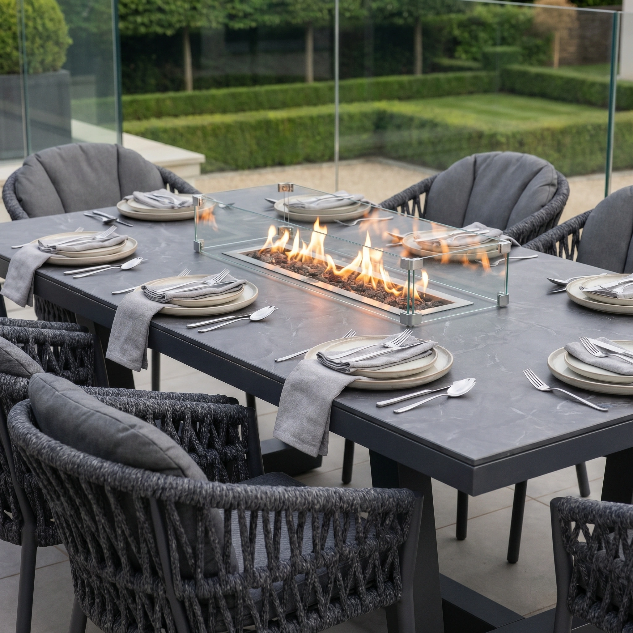 The Pello 8 Seat Rectangular Ceramic Firepit Dining Set in Grey features weather-resistant materials, eight gray chairs, and a built-in glass fire pit centerpiece for stylish and durable outdoor dining.