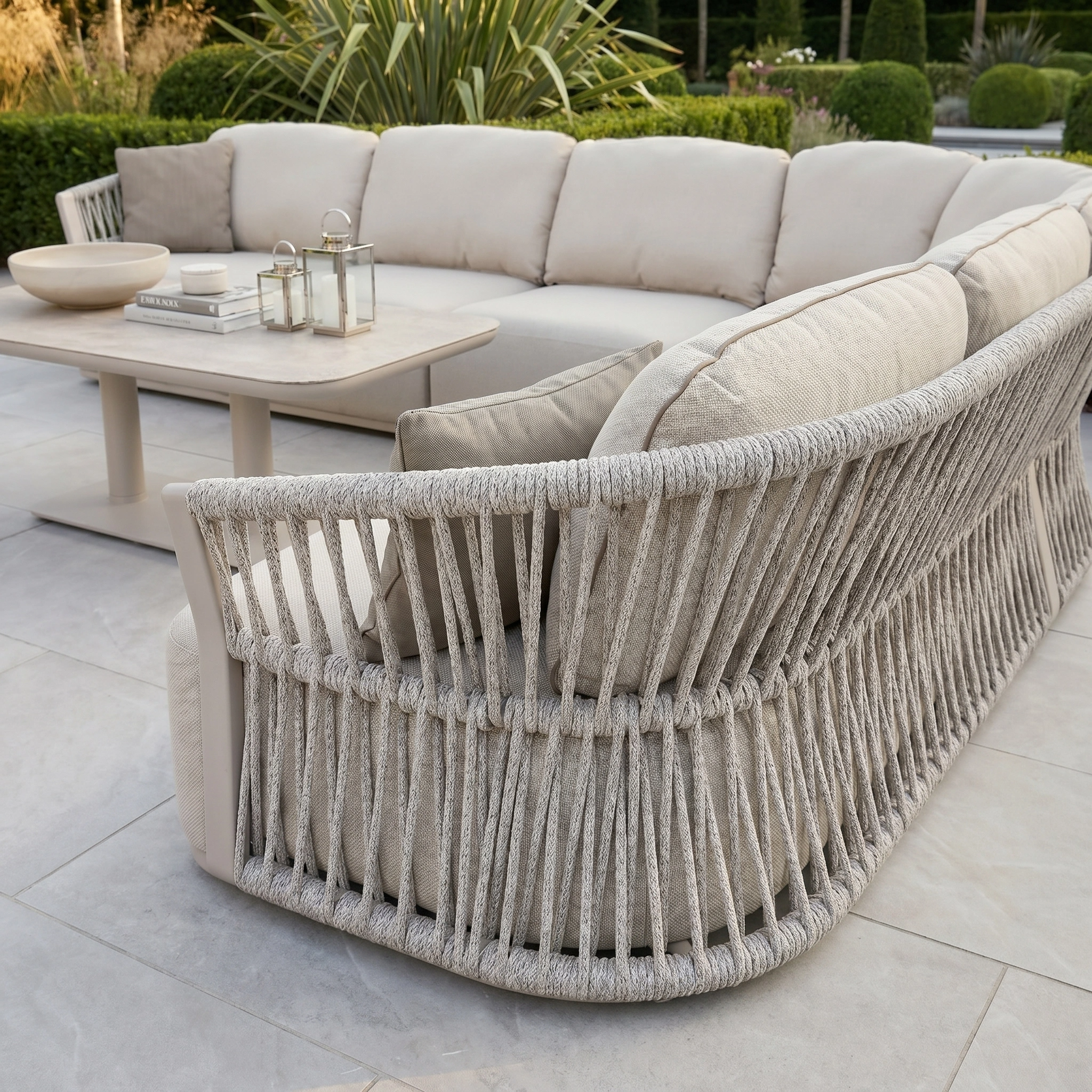 Outdoor patio with the Pello Deluxe Curved Sofa Set in Fawn, featuring rope detail, quick dry cushions, and an Altura Rising Table decorated with lanterns and a bowl.