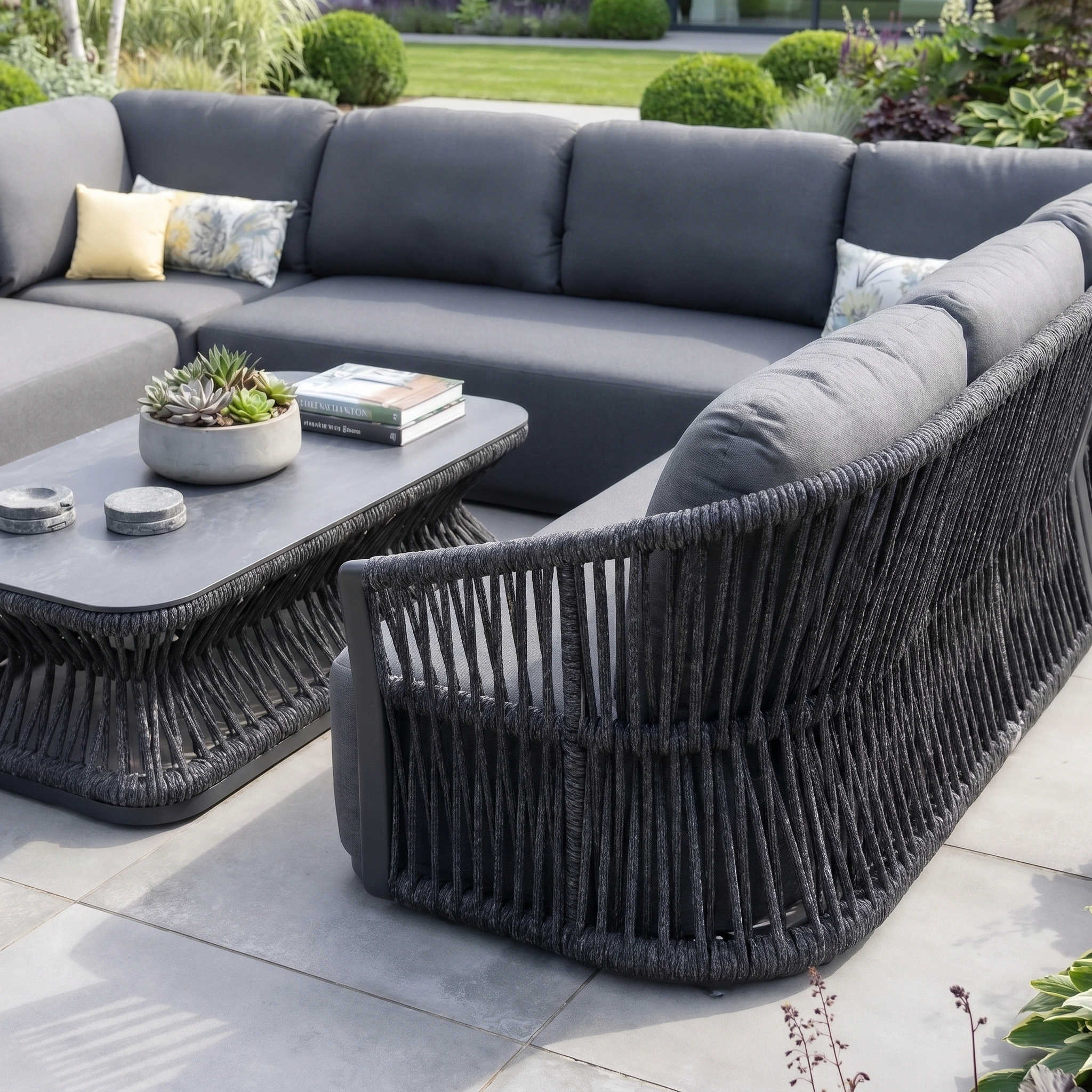 Outdoor patio with the Pello U-Shape Corner Sofa Set in grey, featuring cushioned seats, a rectangular coffee table, and decorative plants on tiled flooring.