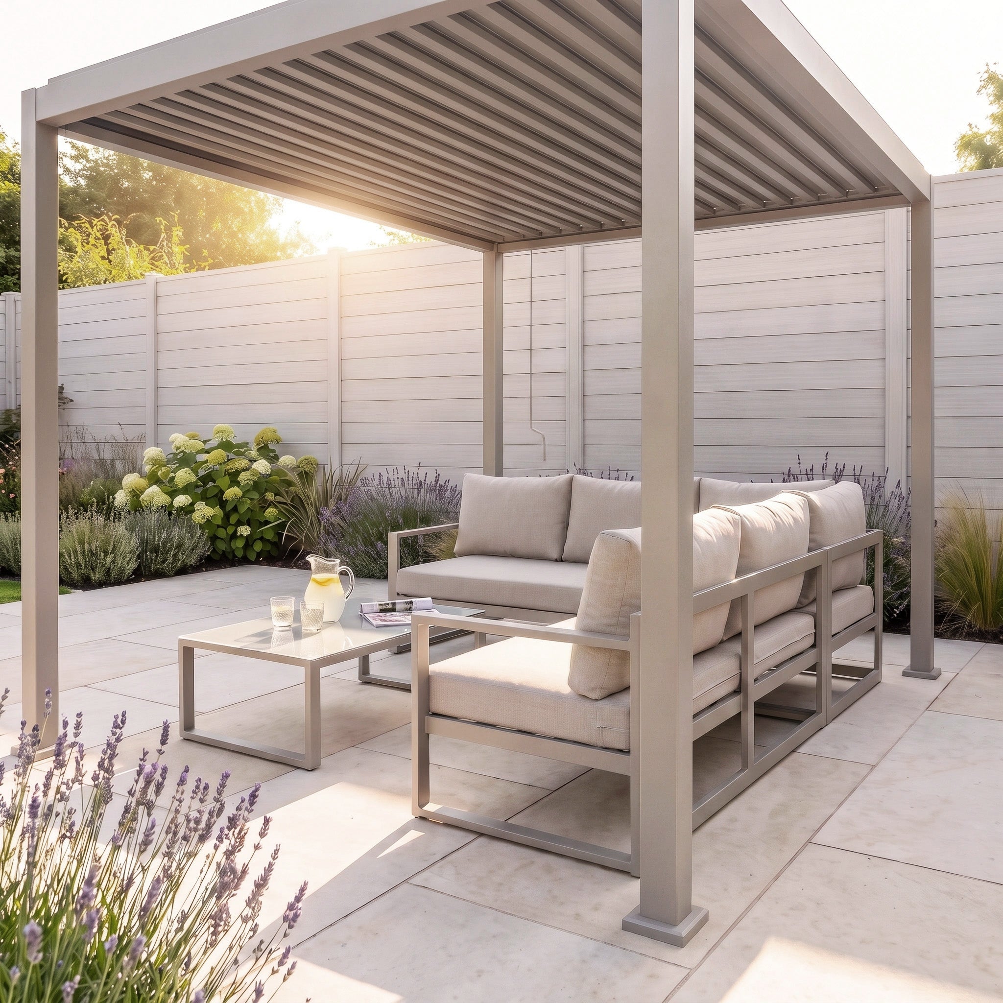 Modern patio featuring two cushioned sofas and a table with lemonade, all arranged beneath the PergoSTET Lite 2.4m x 3m Metal Rectangular Pergola in Latte with tilting louvres, creating an inviting outdoor shelter in a sunny garden.