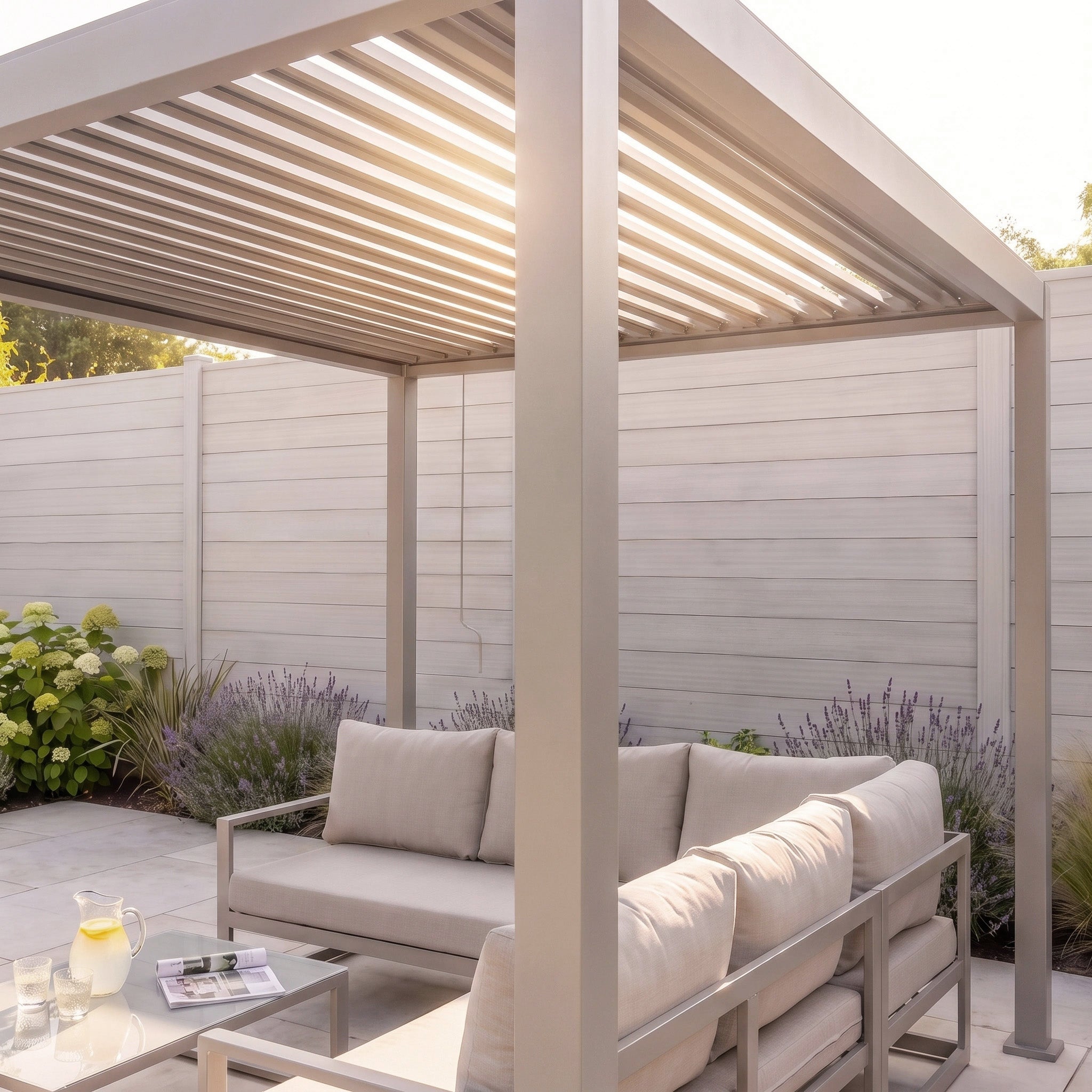 Modern patio with the PergoSTET Lite 2.4m x 3m Metal Rectangular Pergola in Latte, featuring tilting louvres, an outdoor sofa, a table with a pitcher, and sunlight streaming through the slatted roof for comfortable outdoor shelter.