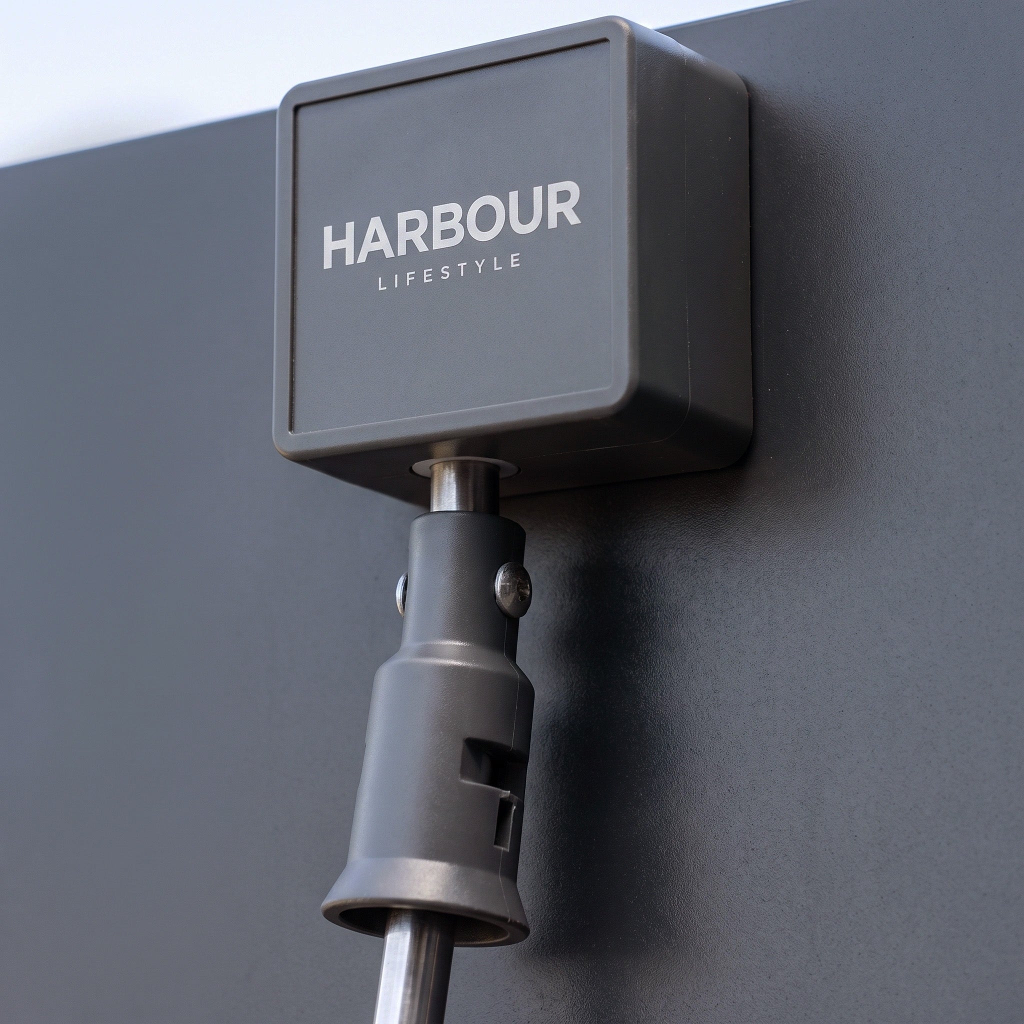 Close-up of a grey device labeled "HARBOUR LIFESTYLE" mounted on a dark vertical surface, featured as part of the PergoSTET Lite 2.4m x 3m Metal Rectangular Pergola in Grey, which includes tilting louvres for adjustable outdoor shade.