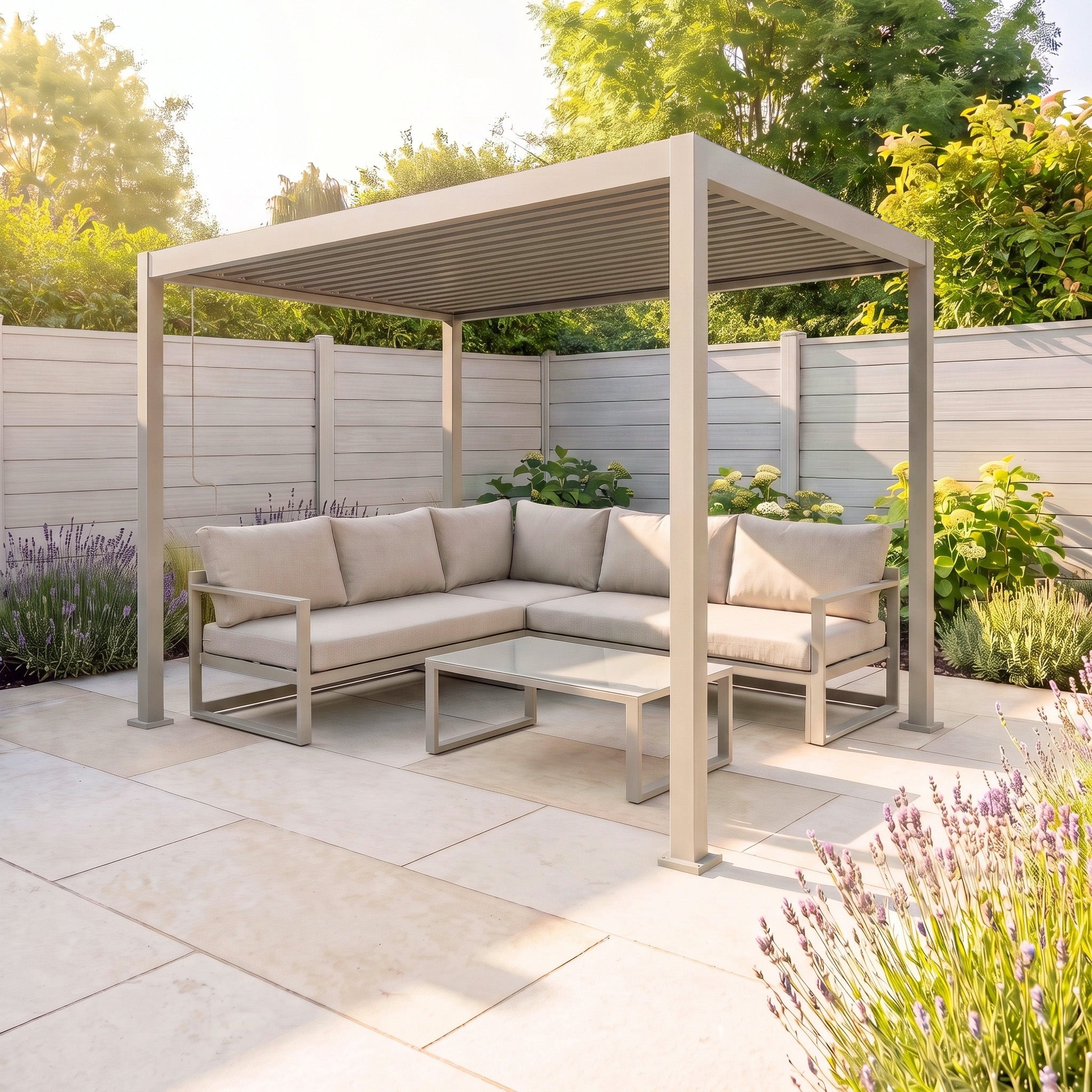 Modern patio with a beige outdoor sofa, glass table, and the PergoSTET Lite 2.4m x 3m Metal Rectangular Pergola in Latte featuring tilting louvres, creating the perfect outdoor shelter amid a lush garden surrounded by a white fence.