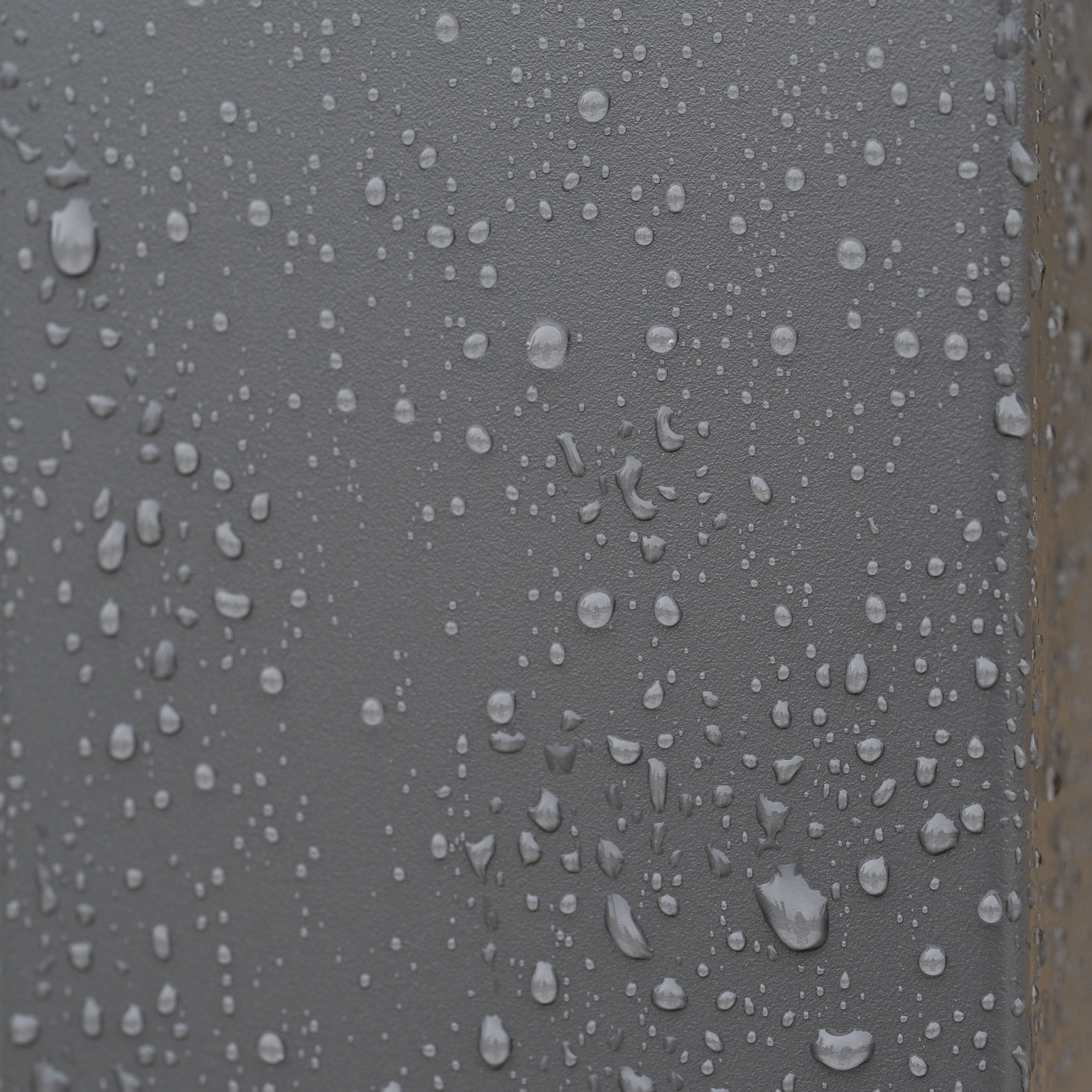 Water droplets on a dark gray surface, showing texture and a bead-like pattern, reminiscent of the refined lines found on the PergoSTET Lite 2.4m x 3m Metal Rectangular Pergola in Grey with tilting louvres designed for outdoor shade.