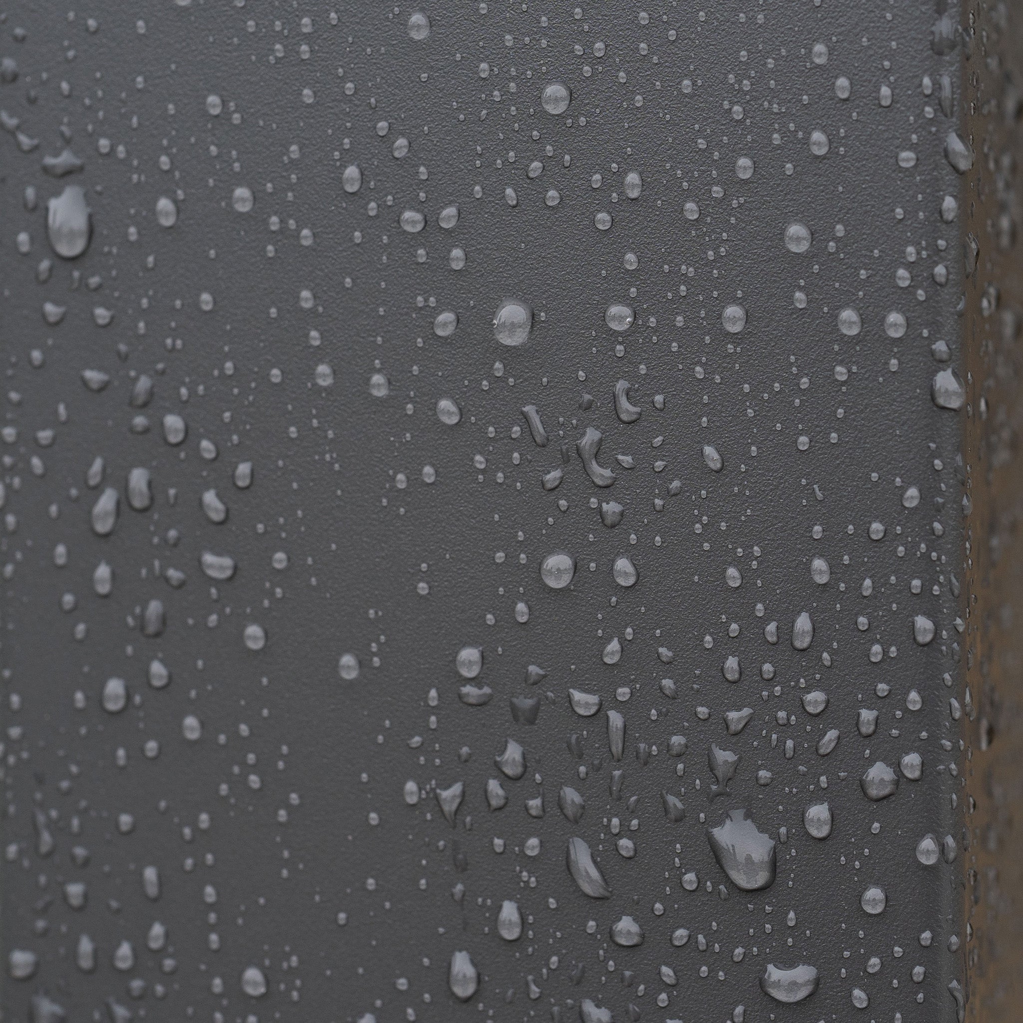 Water droplets on the dark grey surface of the PergoSTET Lite 2.4m x 3m Metal Rectangular Pergola, with some droplets running down near the corner edge—an effect often seen after rain gathers on the tilting louvres of this outdoor shade structure.