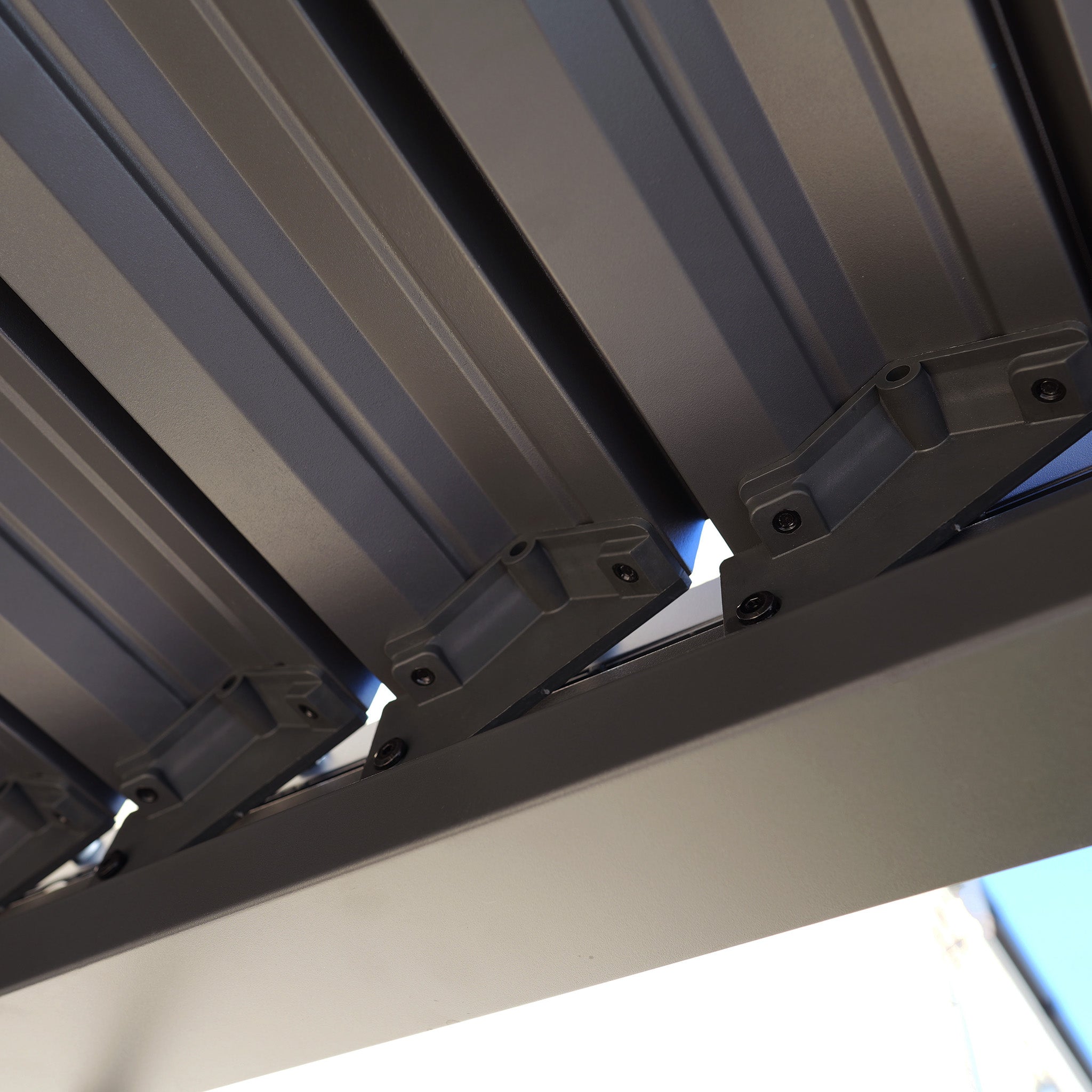 Close-up view of gray metal slats and brackets from the PergoSTET Lite 2.4m x 3m Metal Rectangular Pergola in Grey, featuring tilting louvres for adjustable outdoor shade as part of its modern architectural design.