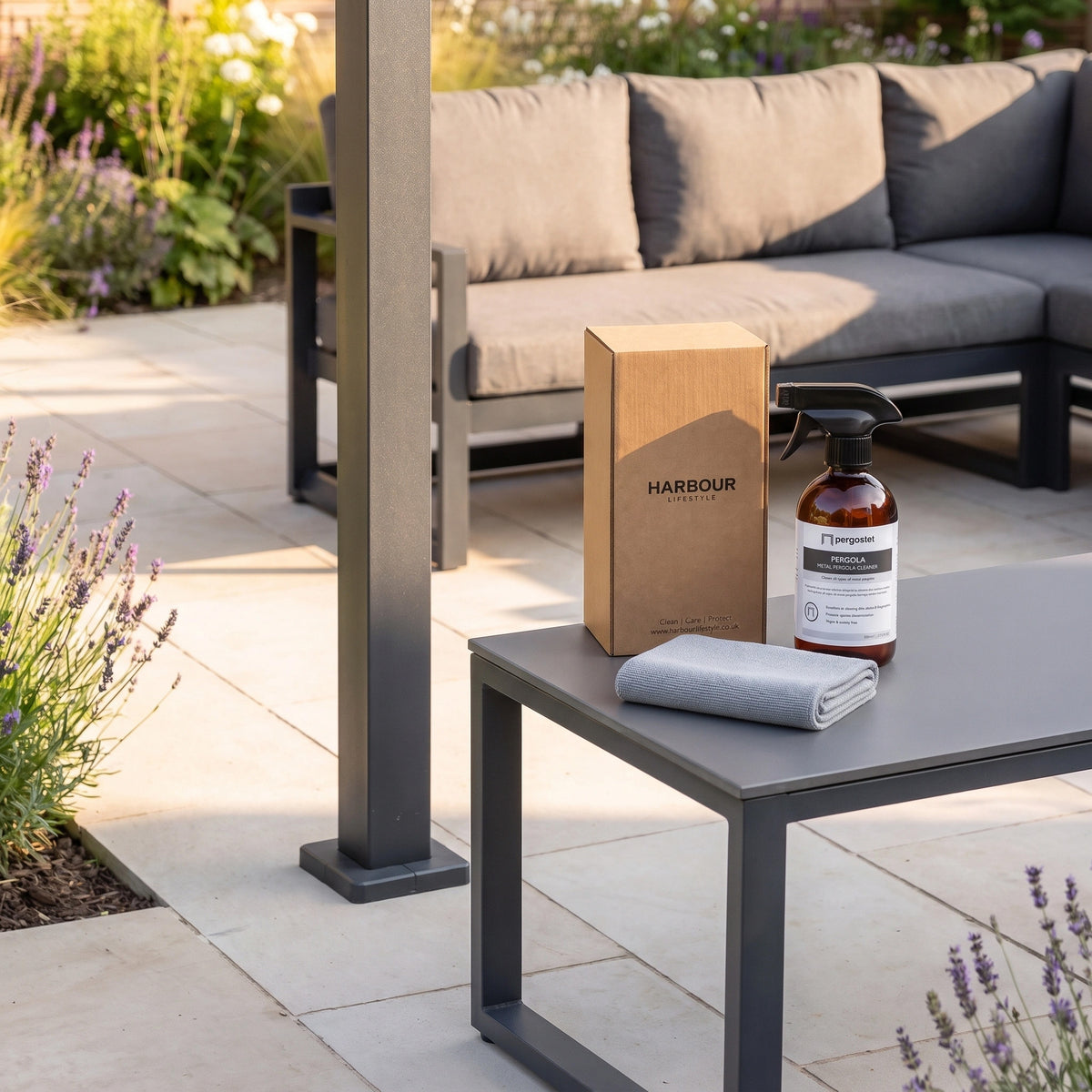 Outdoor Aluminium and Steel Pergola Cleaner spray bottle, box, and cloth on an outdoor coffee table beside a grey sofa—perfect for keeping your metal pergola looking pristine.