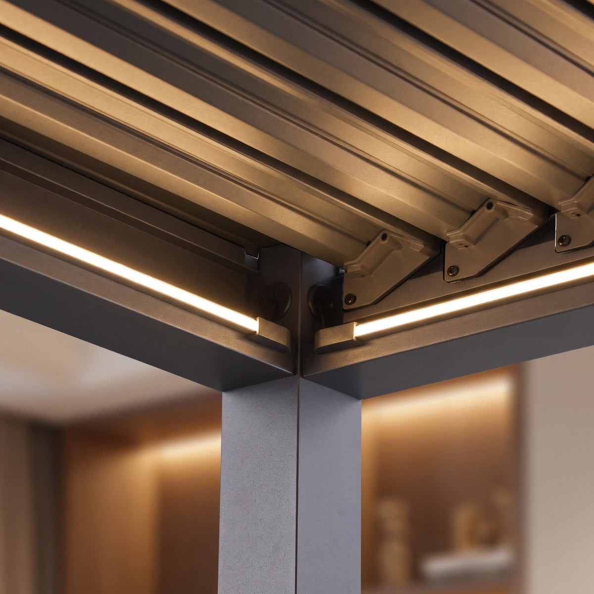 Close-up of the PergoSTET Lite 3m x 4m Metal Rectangular Pergola in Grey, featuring integrated LED lighting and motorised louvres, shown indoors with a blurred background.