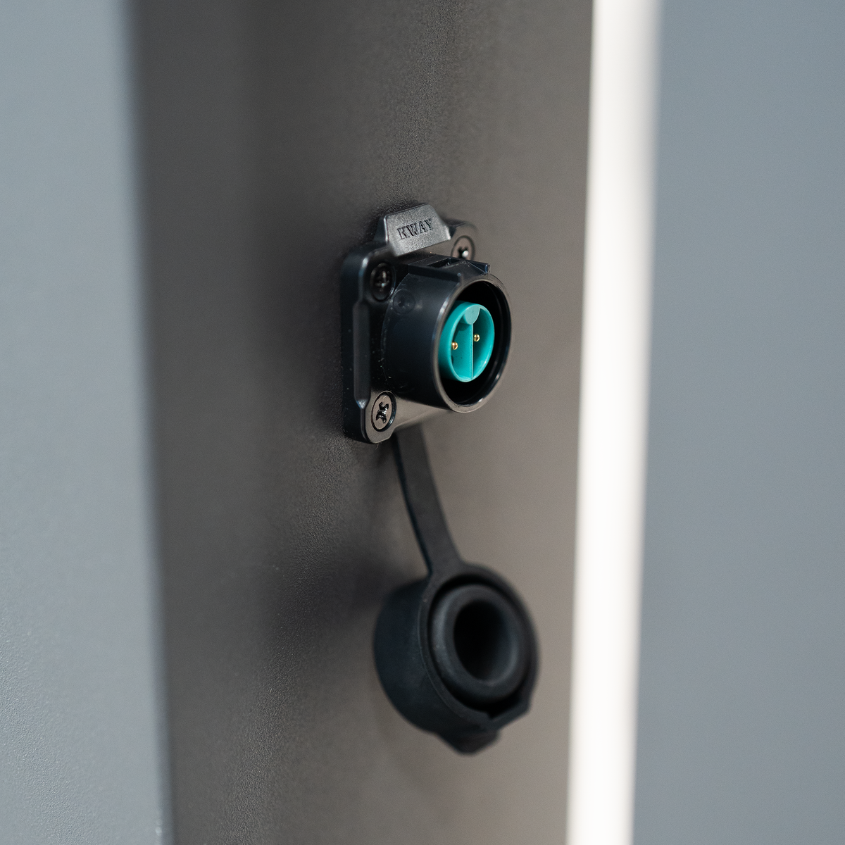 Close-up of a black electrical socket with two green holes and a black rubber protective cap, mounted on the wall—ideal for powering features like LED lighting within the PergoSTET Lite 3m x 4m Metal Rectangular Pergola With Motorised Louvres and LED Lighting in Grey, providing reliable outdoor power beneath its motorised louvres.