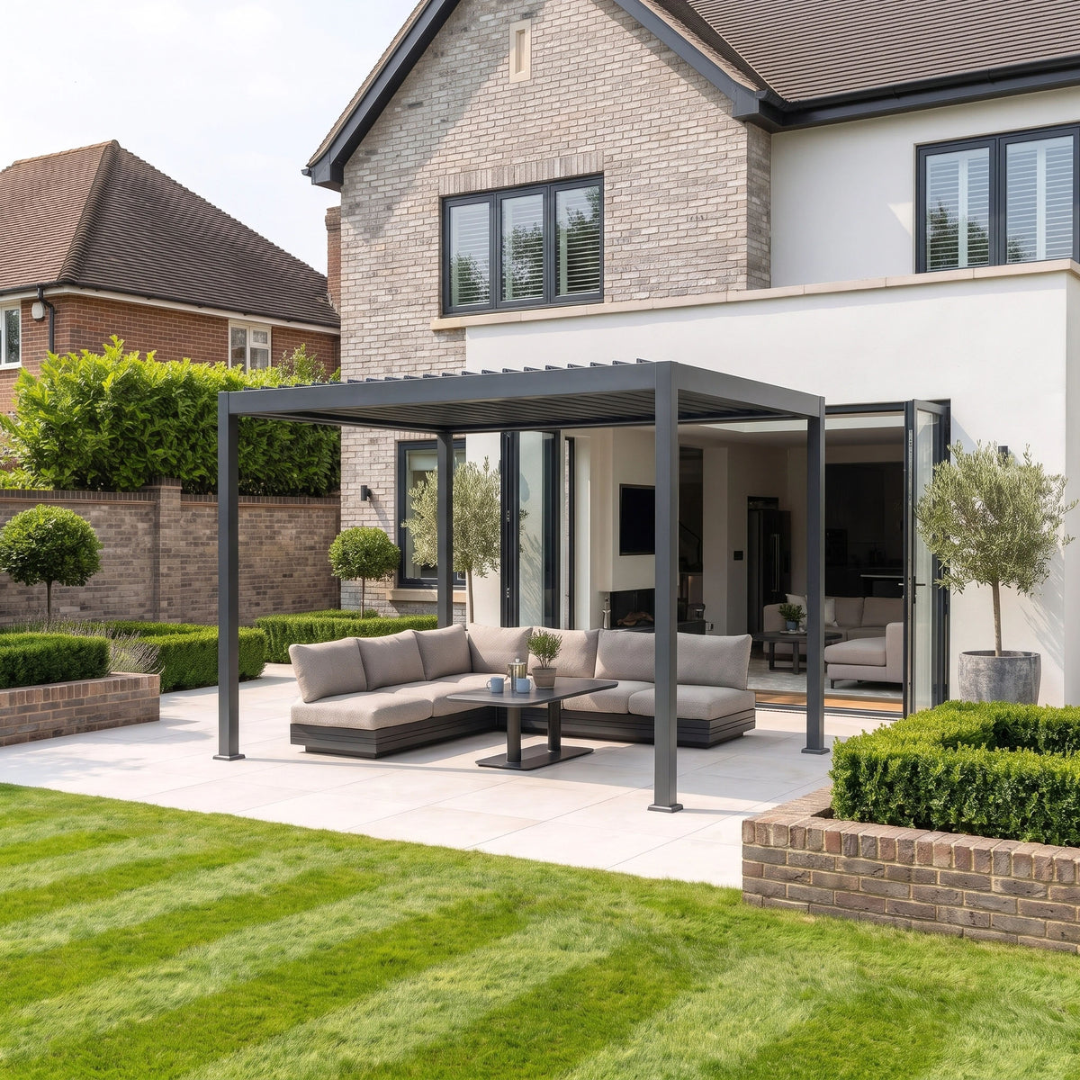 Modern patio with a PergoSTET Lite 3m x 4m Metal Rectangular Pergola featuring motorised louvres and integrated LED lighting in grey, complemented by an outdoor sofa, table, and a manicured lawn in front of a contemporary house.