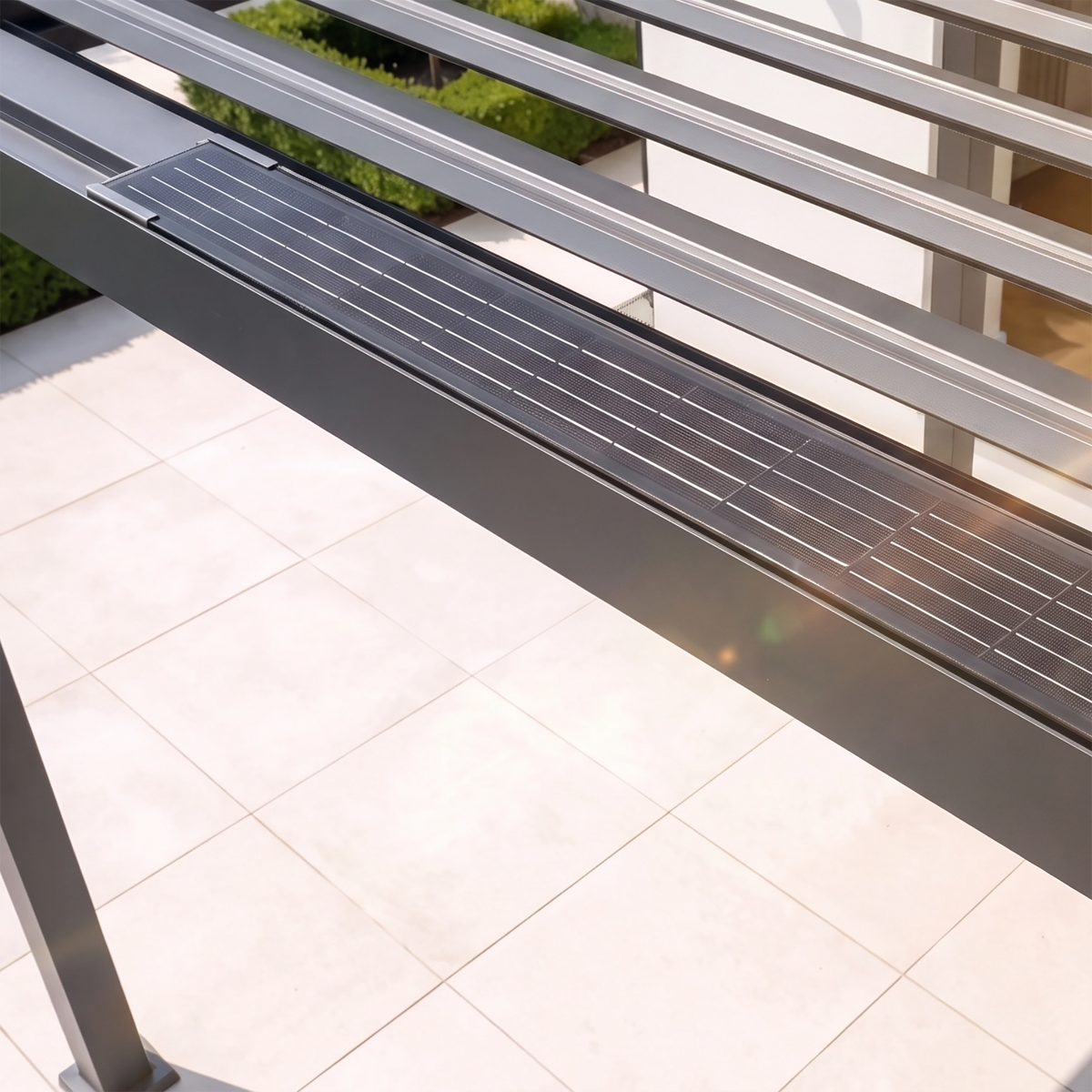 Close-up of the PergoSTET Lite 3m x 4m Metal Rectangular Pergola with motorised louvres and LED lighting in grey, featuring solar panels installed above a tiled patio in sunlight.