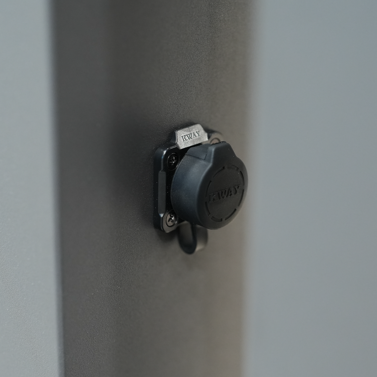 Close-up of a black, round wall-mounted lock cover with “KWAY” embossed on the cap, stylishly complementing modern upgrades such as the PergoSTET Lite 3m x 4m Metal Rectangular Pergola with motorised louvres and integrated LED lighting in grey.