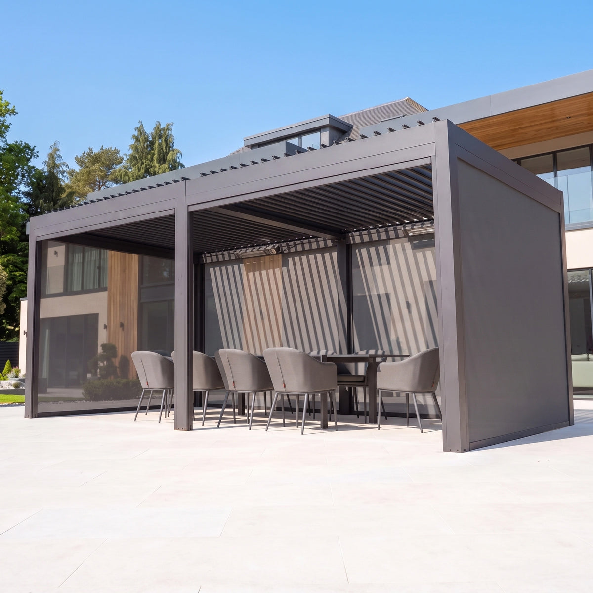 PergoSTET Deluxe 3m x 6m grey pergola with motorised louvres, side screens, LED lighting, and outdoor dining set.