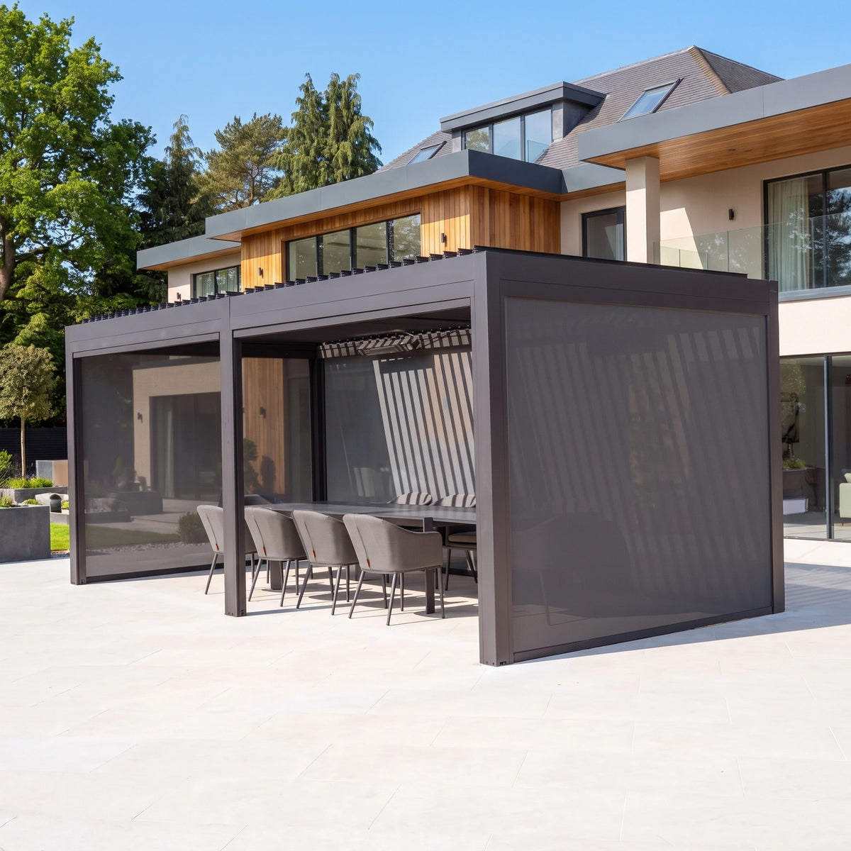 PergoSTET Deluxe 3m x 6m grey pergola with motorised louvres, LED lighting, dining set, and lowered side blinds.