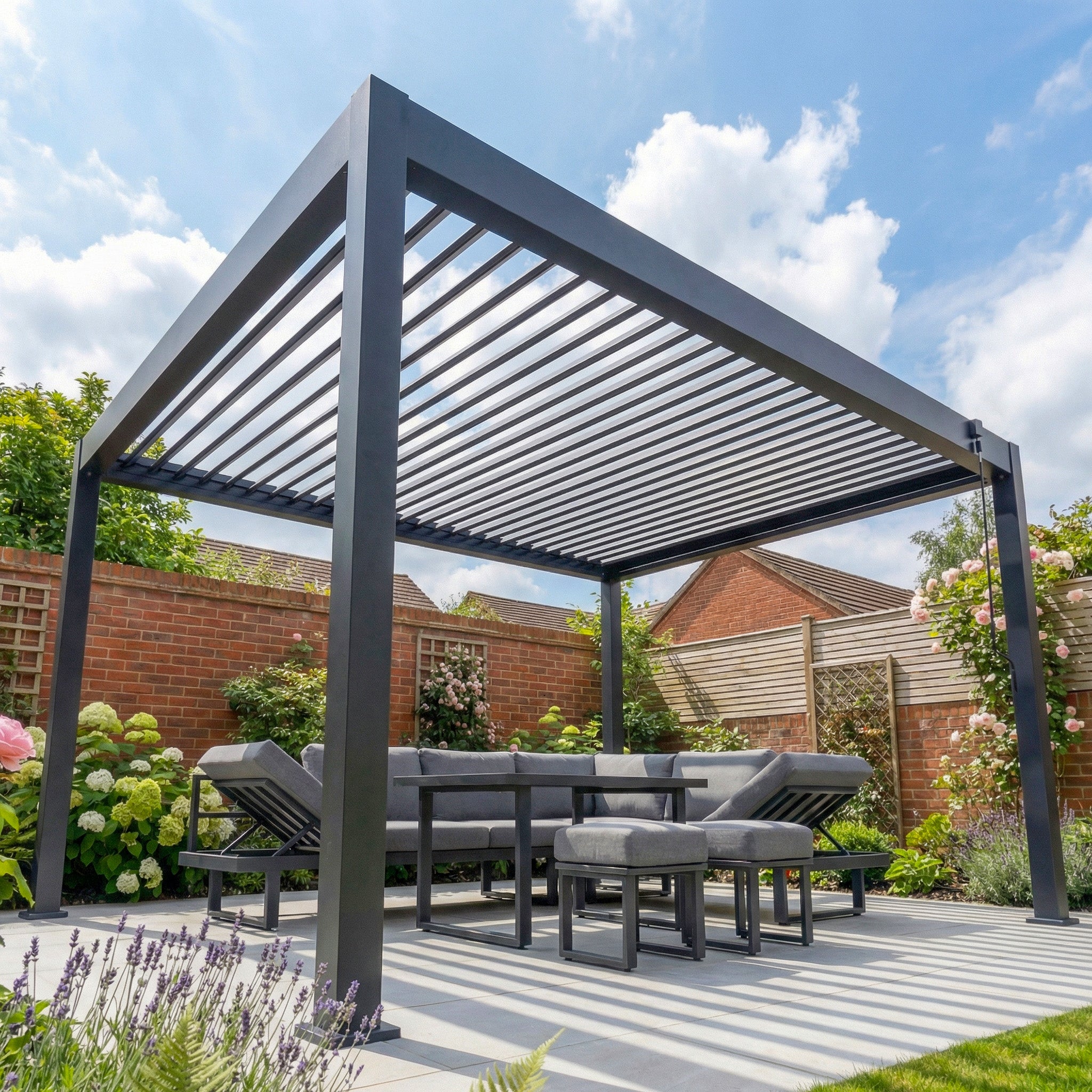The PergoSTET Lite 3m x 4m Metal Rectangular Pergola in Grey features tilting louvres and a seating area, providing flexible outdoor shade amid flowers and greenery in a sunny backyard garden.