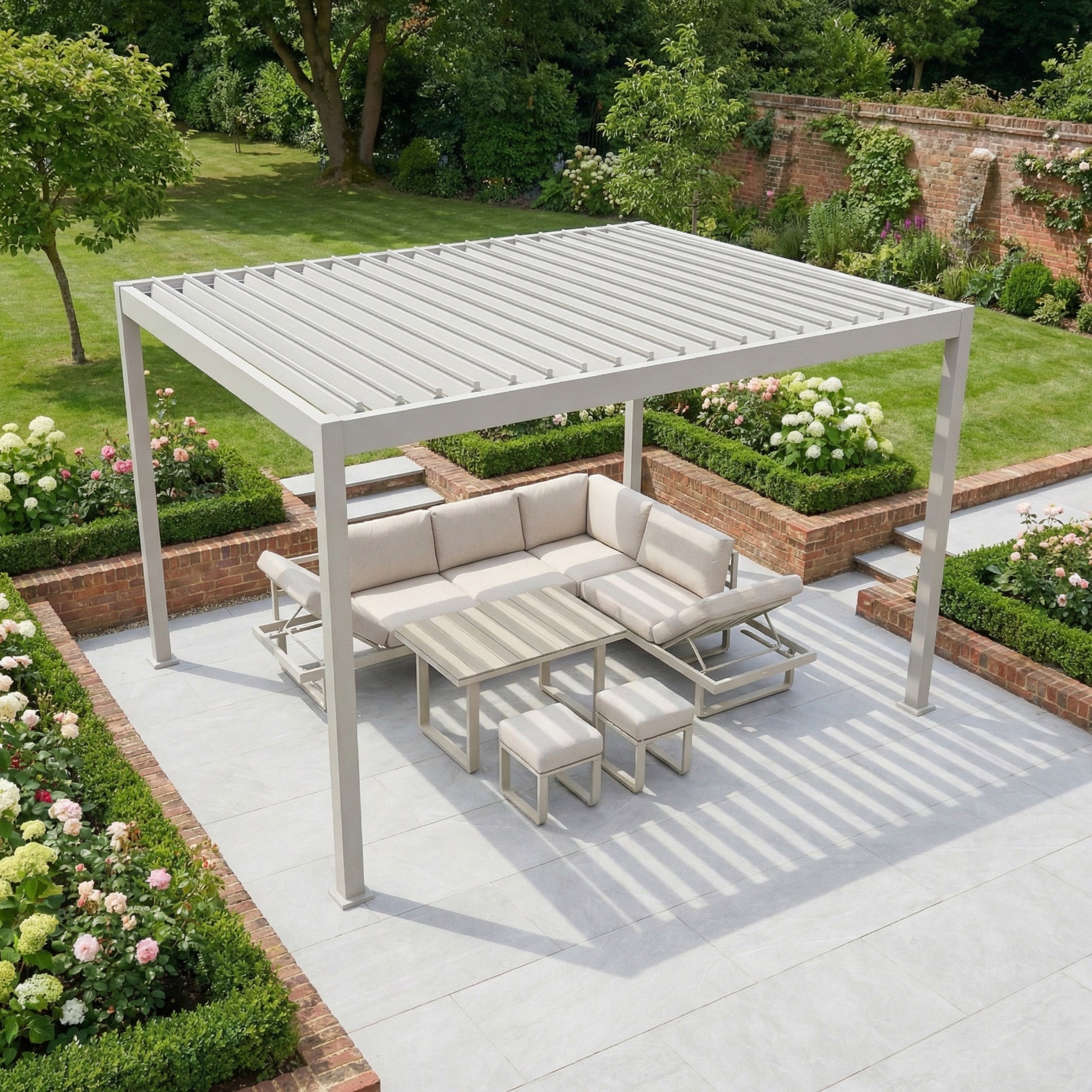 The PergoSTET Lite 3m x 4m Metal Rectangular Pergola in Latte features adjustable louvres for outdoor shade over seating and a table, set amidst a landscaped garden with vibrant flowerbeds.