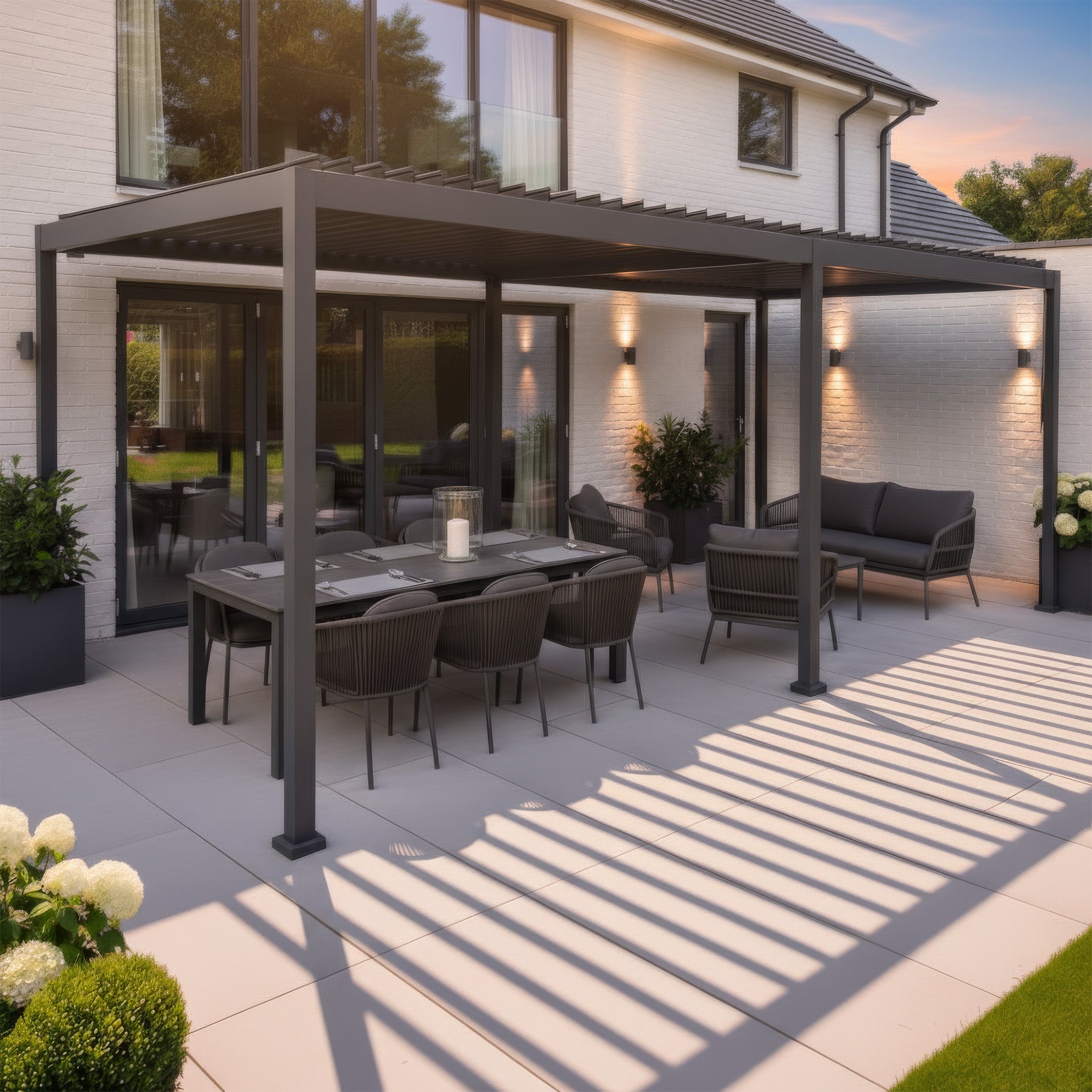A modern patio featuring a dining table, chairs, and the PergoSTET Lite Neo 3m x 7m Metal Rectangular Pergola in Grey casts striped shadows on the tiled floor, creating an inviting outdoor space beside the house.