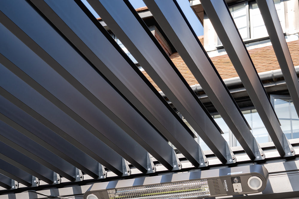 Close-up of CB TEST PRODUCT metal slats creating a pergola roof, with a building and its windows visible in the background.