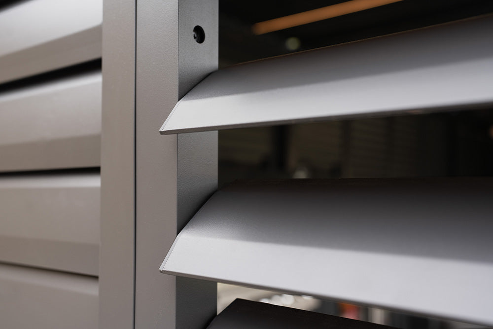 Close-up of angled gray metal louvered panels from CB TEST PRODUCT, with a blurred background partially visible.