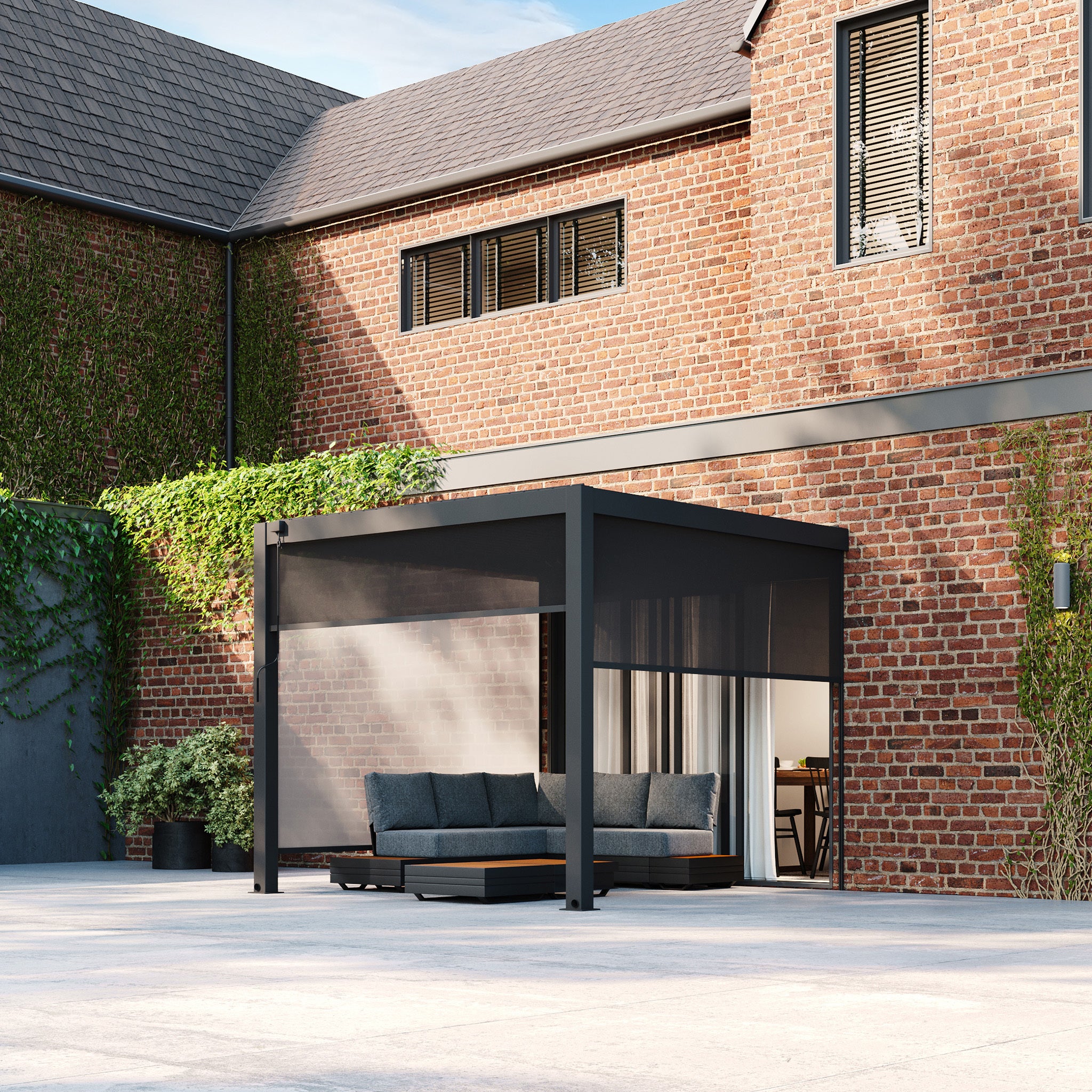 A modern outdoor patio showcases a sleek gray sofa beneath a PergoSTET Plus 3m x 3m Square Wall Mounted Pergola with 3 Drop Sides and LED Lighting in Grey, set against a red brick wall adorned with ivy accents.