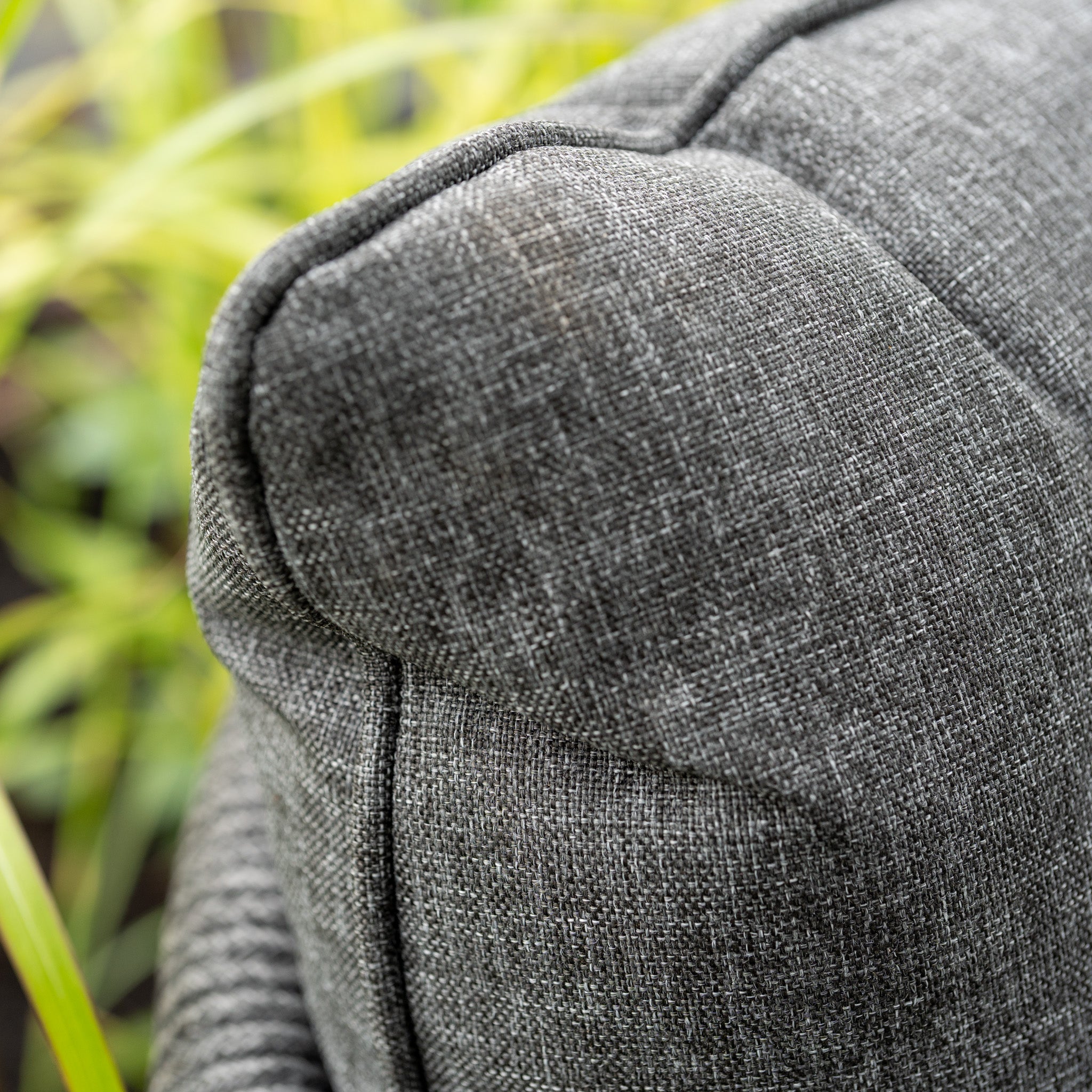 Close-up of the textured grey Rhea 2 Seat Sofa Set, part of a modern garden arrangement, with blurred green plants in the background.