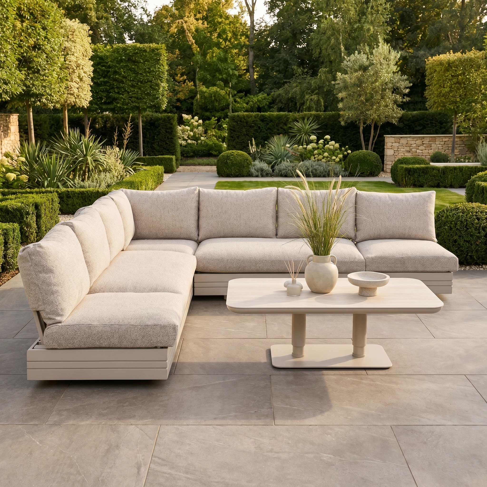 Modern patio showcasing the Savona Luxury Outdoor Large Corner Sofa Set with Altura Rising Table in Oatmeal, set amid a lush green garden backdrop.