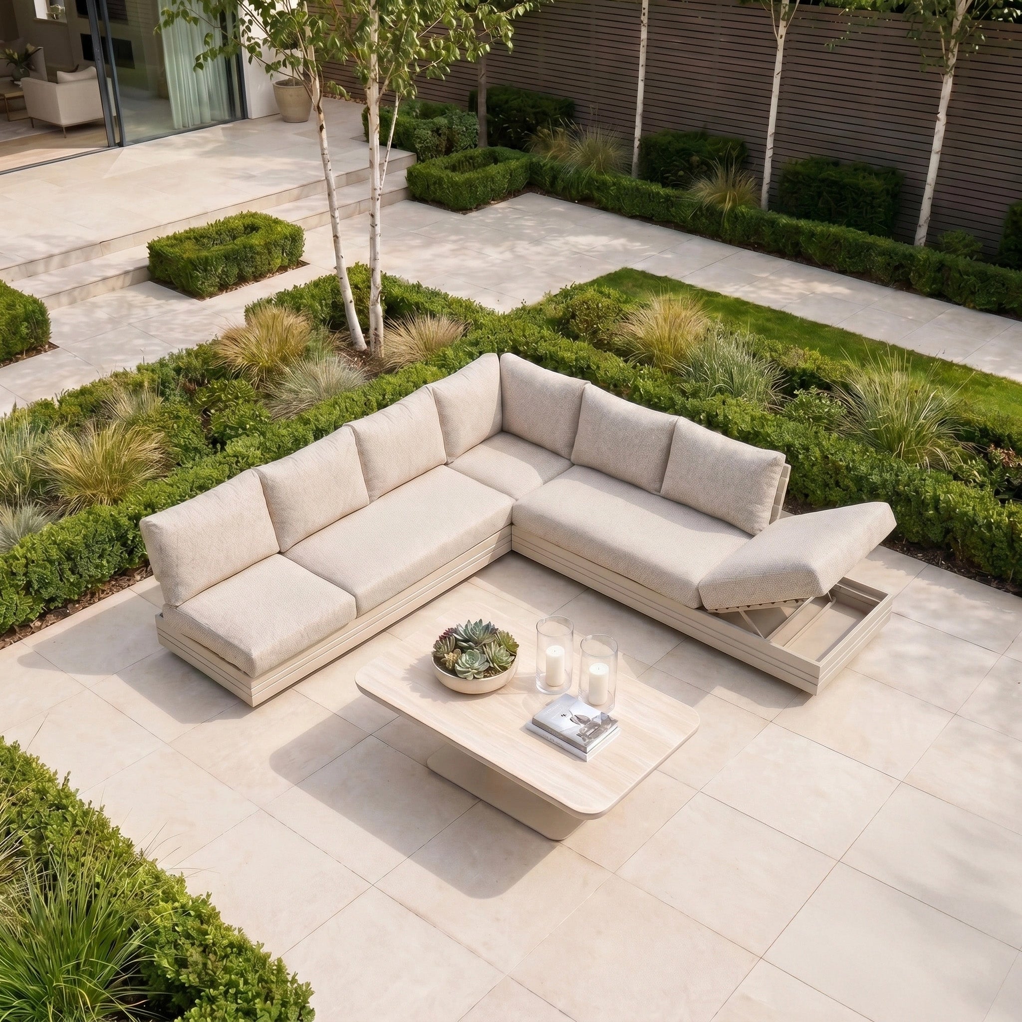 The Savona Luxury Outdoor Large Corner Sofa Set with Altura Rising Table in Oatmeal, set on a patio and surrounded by greenery, is perfect modular garden furniture for stylish relaxation.