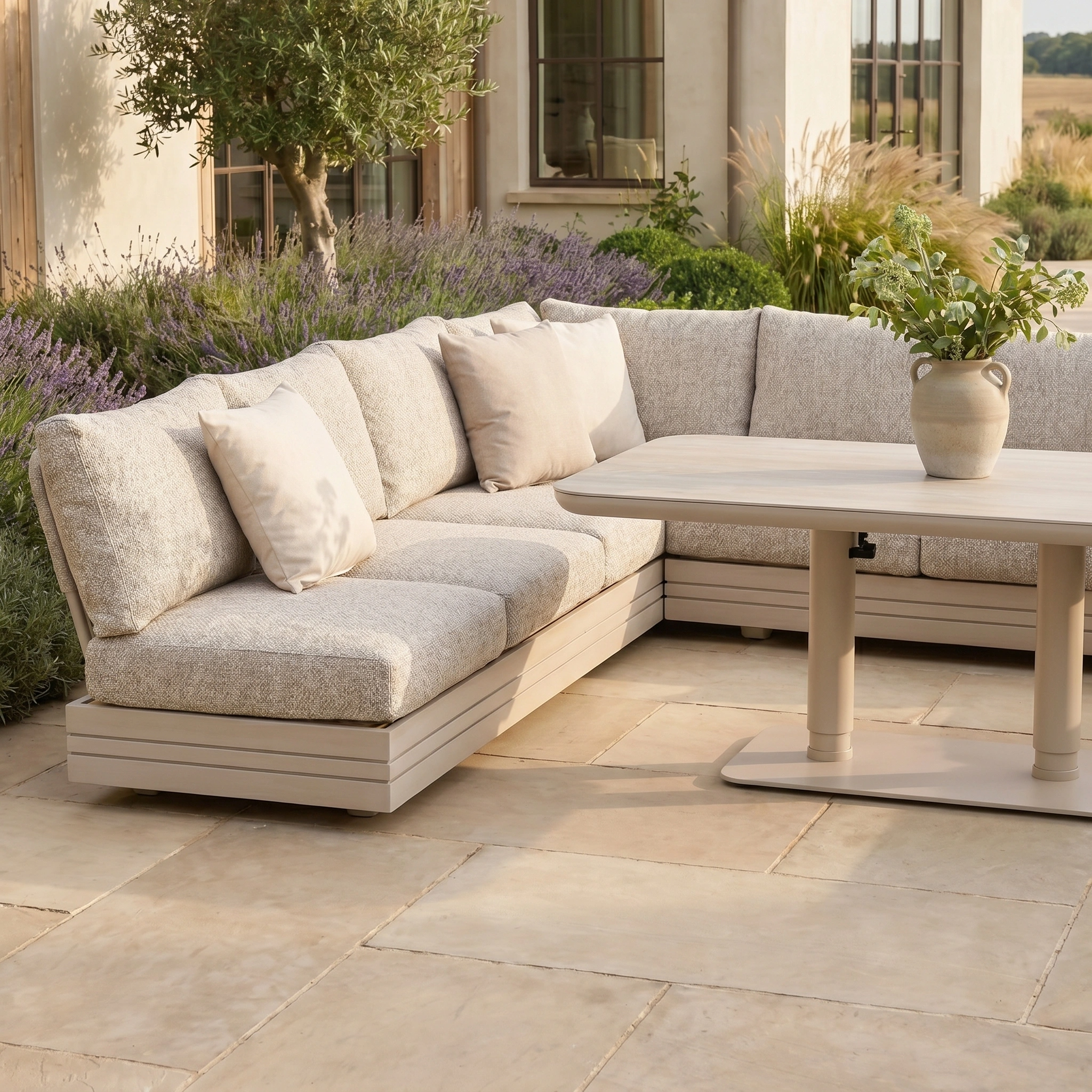 Outdoor patio with the Savona Luxury Outdoor Large U-Shape Corner Sofa Set in Oatmeal and Altura Rising Table, plus a potted plant, surrounded by greenery.