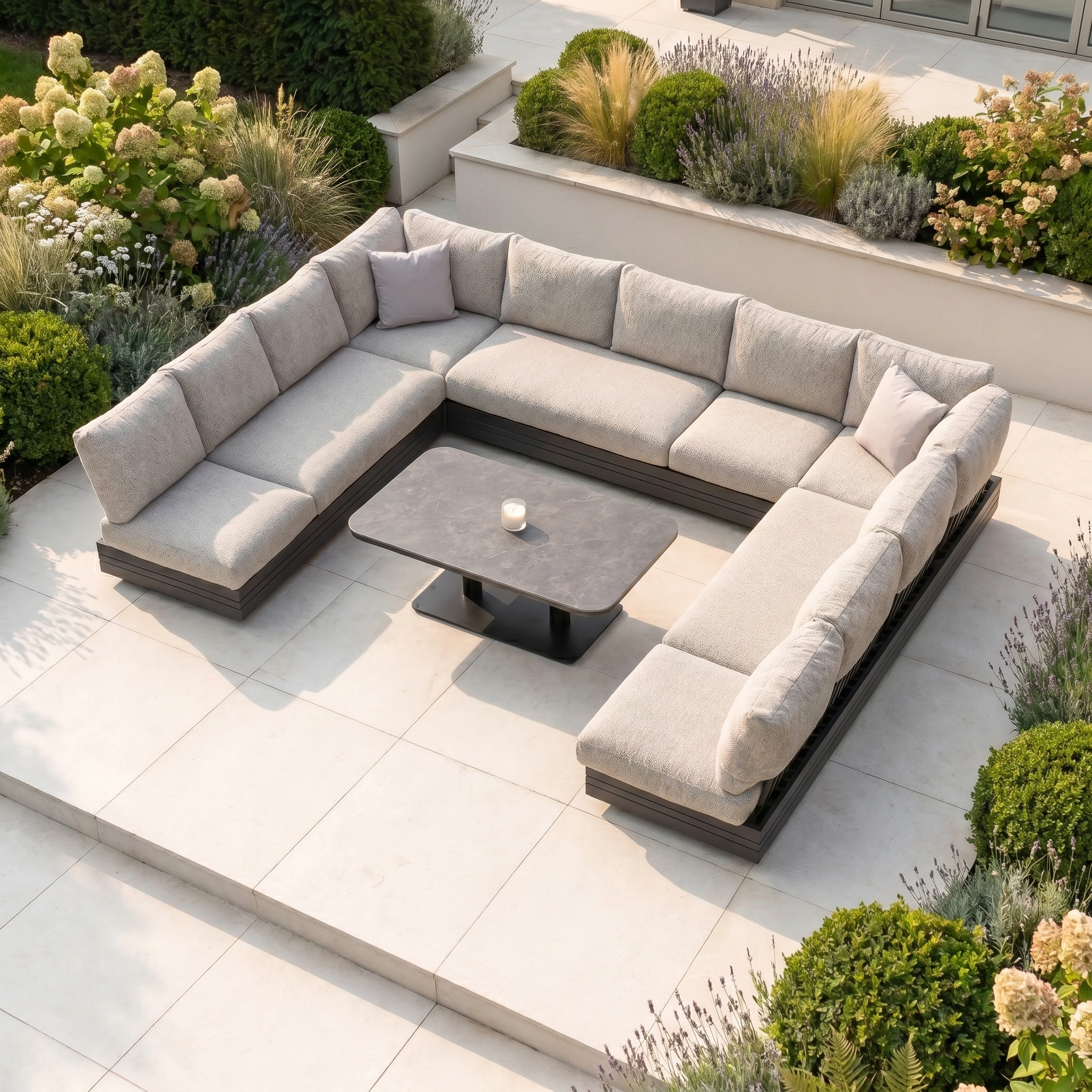The Savona Luxury Outdoor Large U-Shape Corner Sofa Set with Altura Rising Table in Truffle offers stylish comfort on a tiled patio, featuring plush cushions and rust-proof aluminium for modern outdoor luxury surrounded by lush greenery.