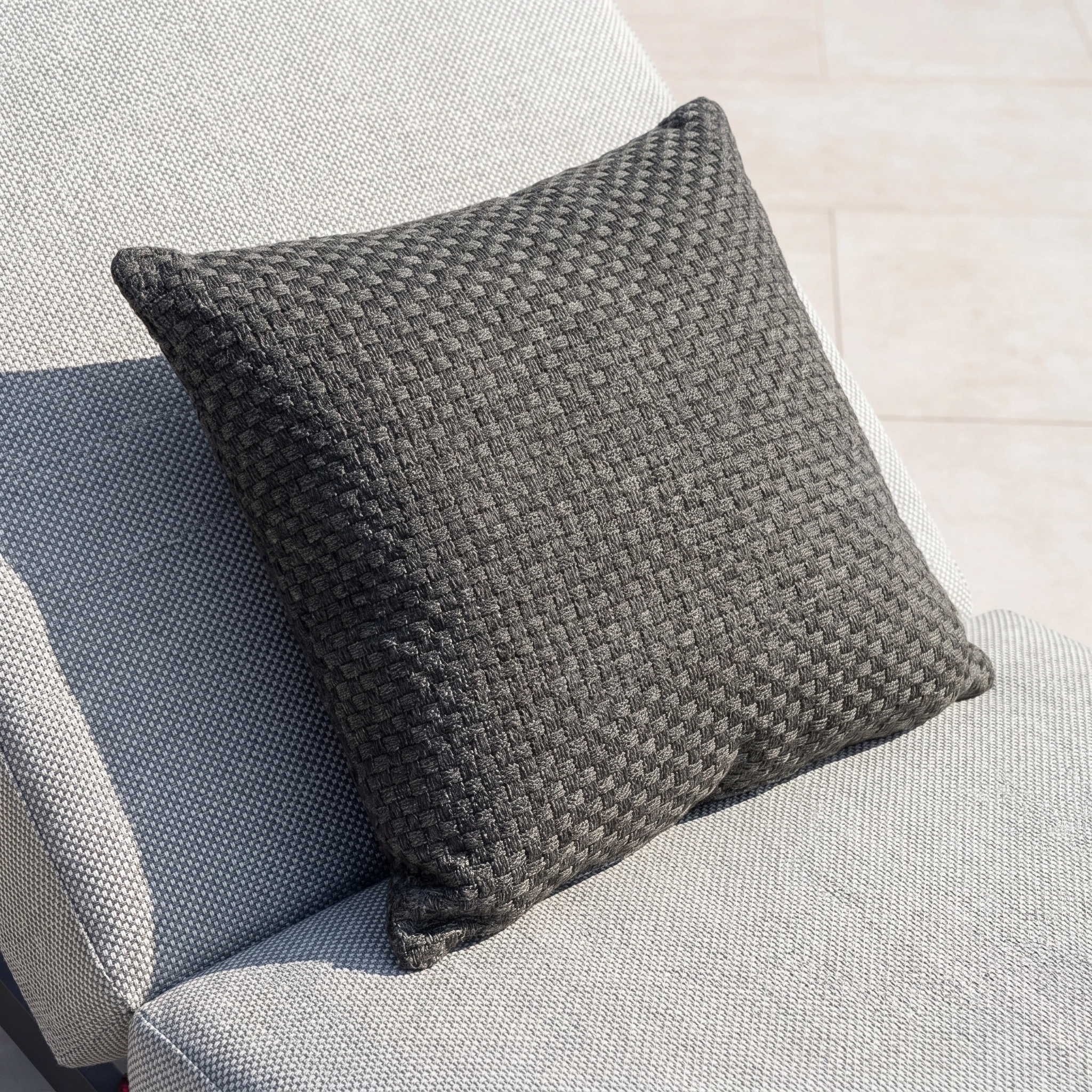 The Agora Senda Grafito Medium Scatter Cushion (45cm x 45cm) in dark grey acrylic adds lasting style and comfort to a light grey textured chair.
