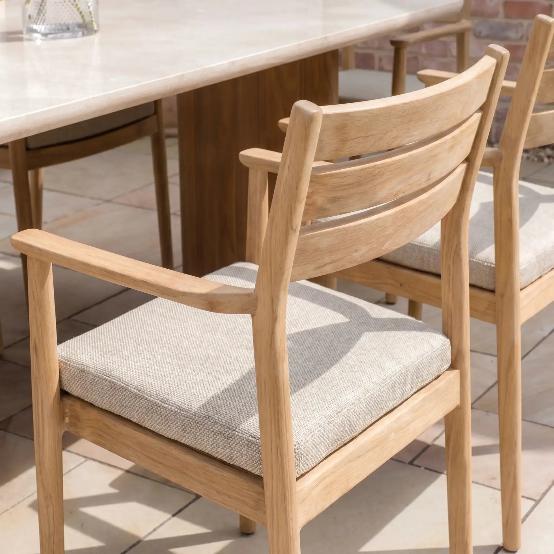 The Siena 6 Seat Dining Set in Fawn features light wooden chairs with cushioned seats placed beside a marble dining table on a tiled floor.