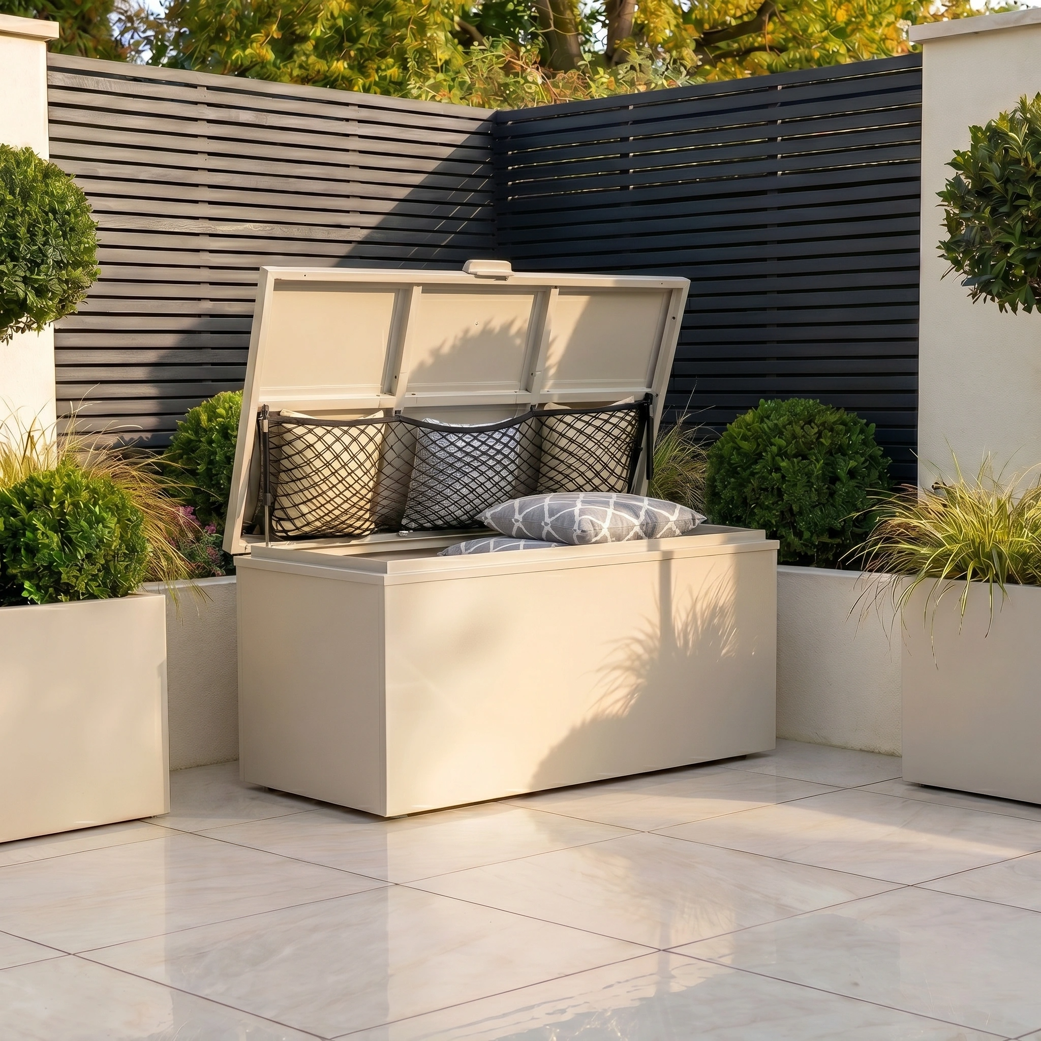 A Small Storage Box in Latte sits open on a tiled patio, revealing cushions inside and surrounded by potted plants.