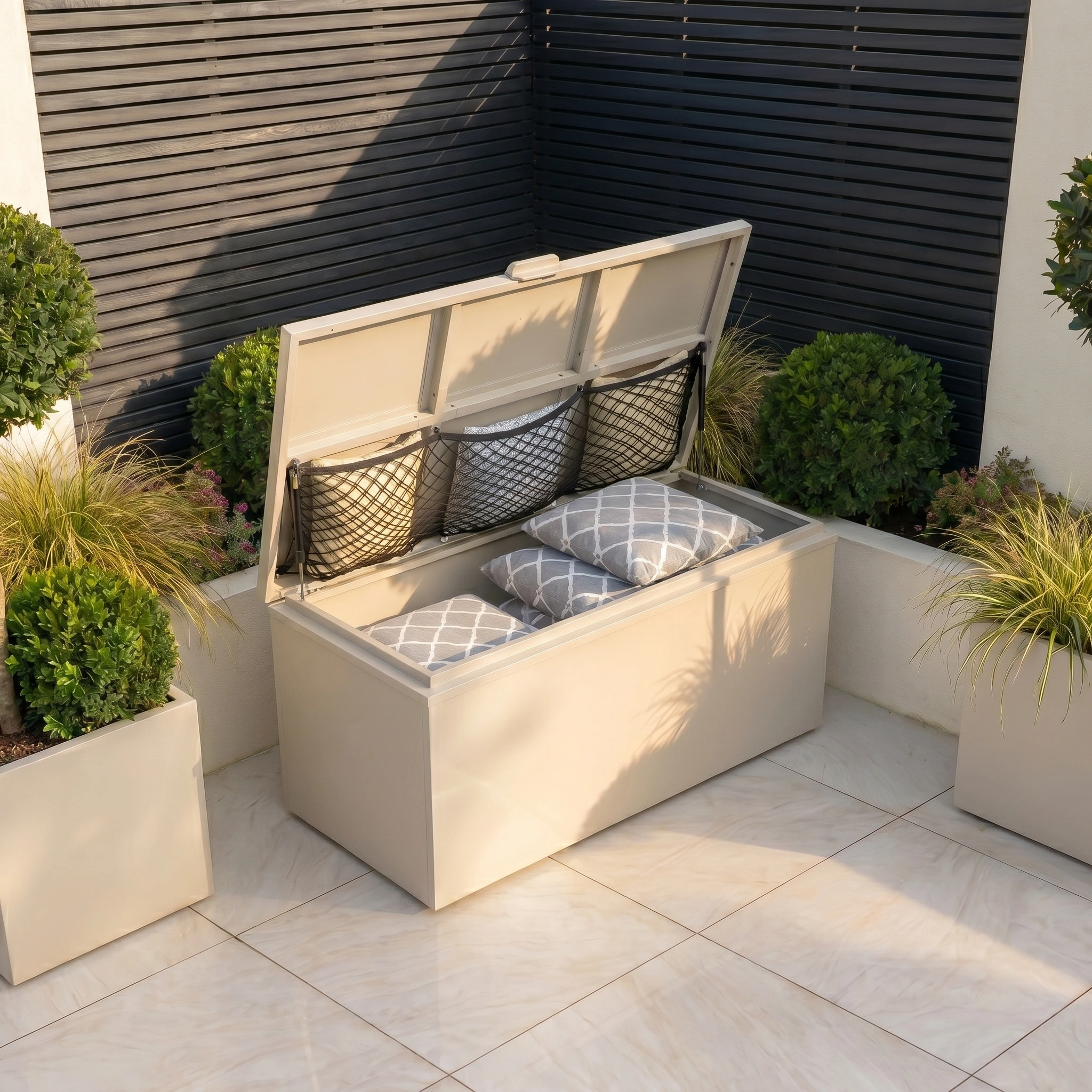 Small Storage Box in Latte with open lid, holding patterned cushions and surrounded by potted plants on a tiled patio.