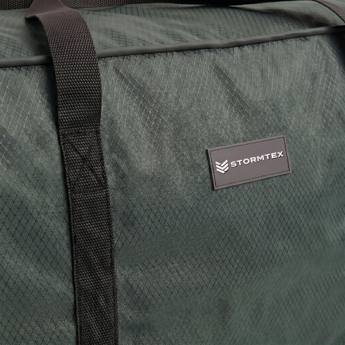 Close-up of a green Stormtex Cushion Storage Bag 145 x 100 x 100cm featuring black straps and a textured surface.