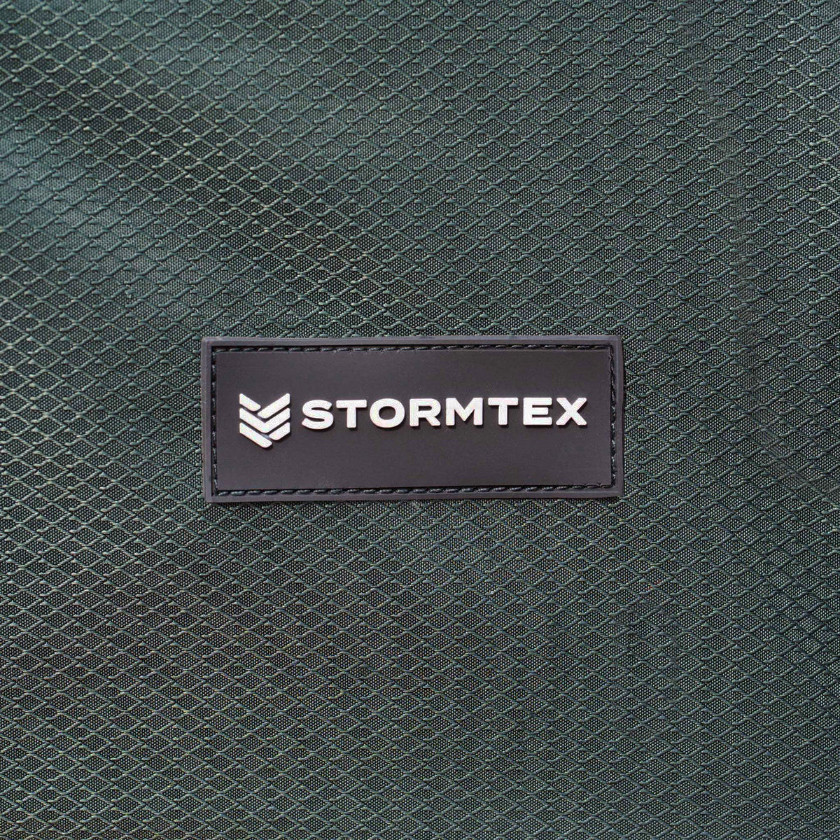 Close-up of a textured green fabric with a black patch labeled “STORMTEX” in white letters, highlighting the durable material used for the Stormtex Cushion Storage Bag 168 x 82 x 95cm—an ideal solution for long cushion storage.