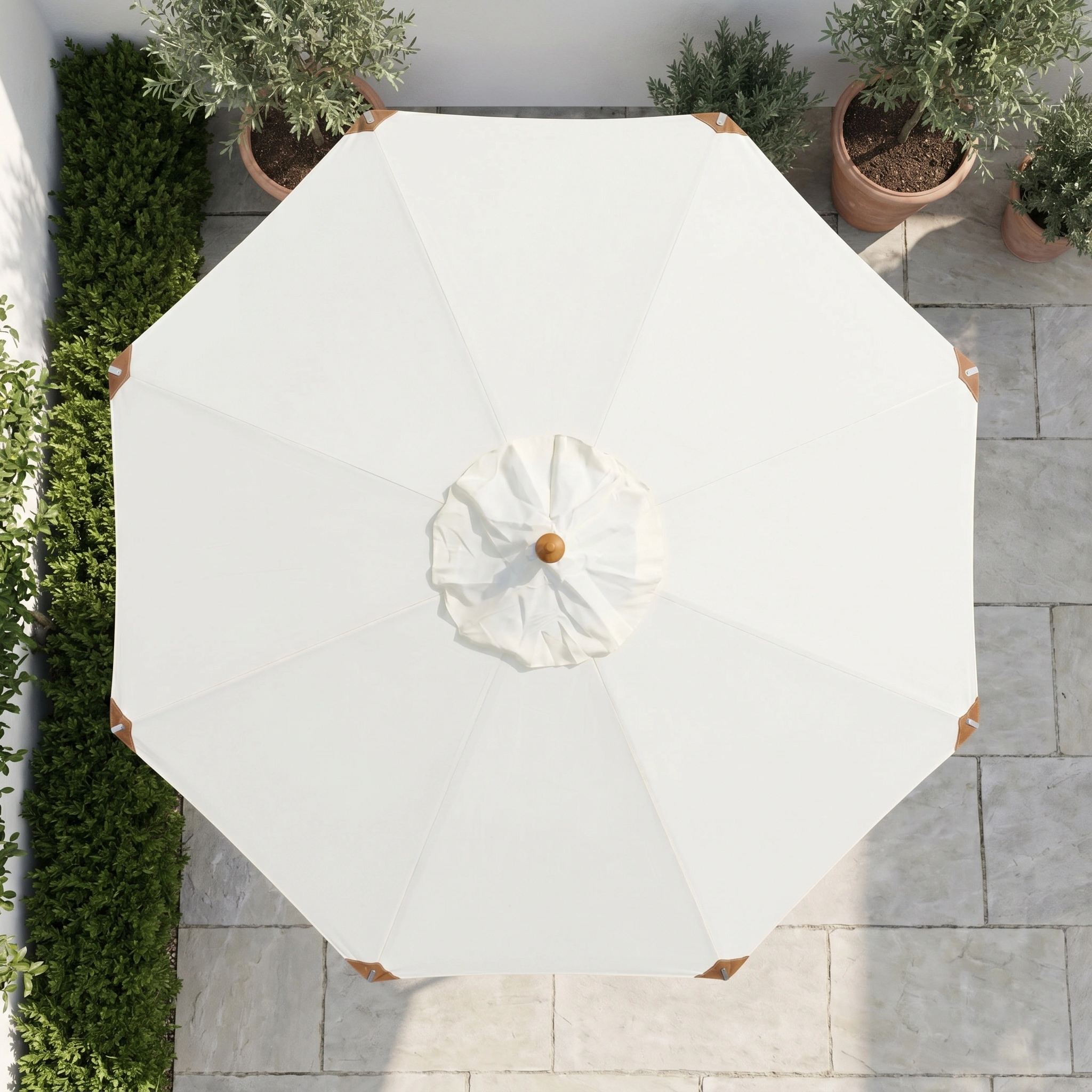 Top view of the Styx 3m Round Deluxe Wooden Parasol in Beige on a stone tile patio, surrounded by green plants and potted trees.